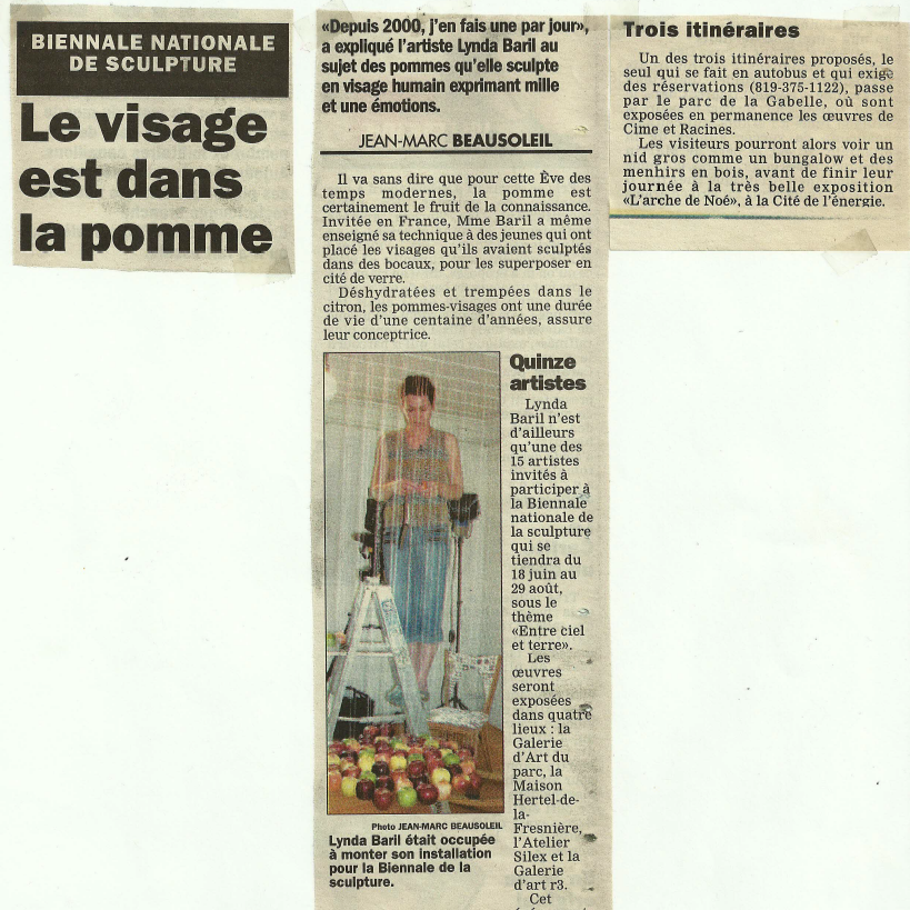 Article de presse en français parlant de la Biennale nationale de sculpture, avec une image d'une artiste debout devant une installation de sculptures représentant des pommes. La légende indique que Lynda Baril, l'artiste, était en train de monter son installation.