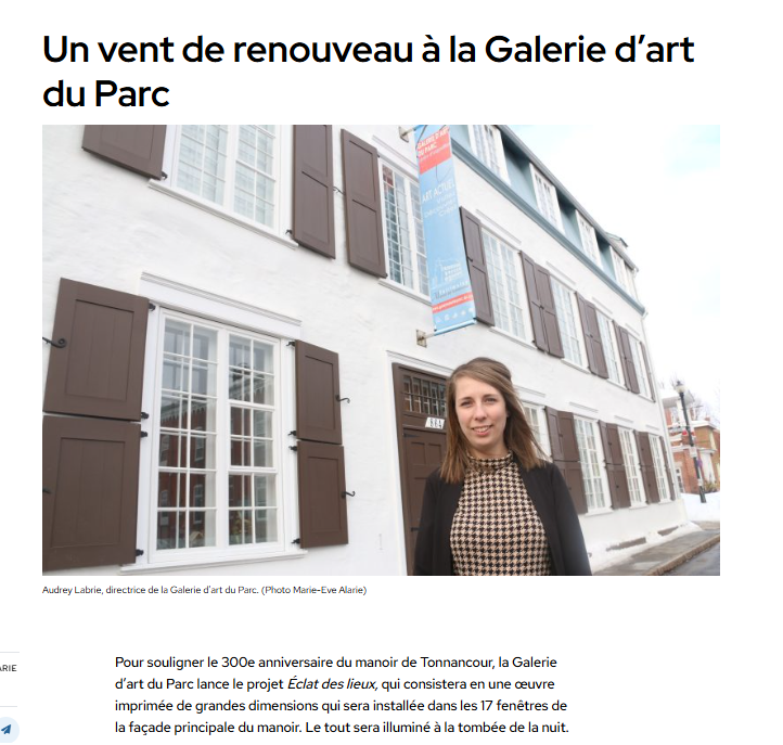 Une femme debout devant un bâtiment blanc avec volets bruns, à l'extérieur, lors d'une journée ensoleillée.