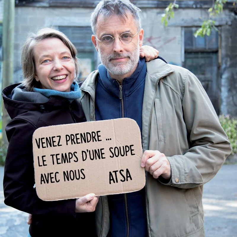 Deux personnes tiennent une pancarte en carton qui dit Venez prendre... Le temps d'une soupe avec nous