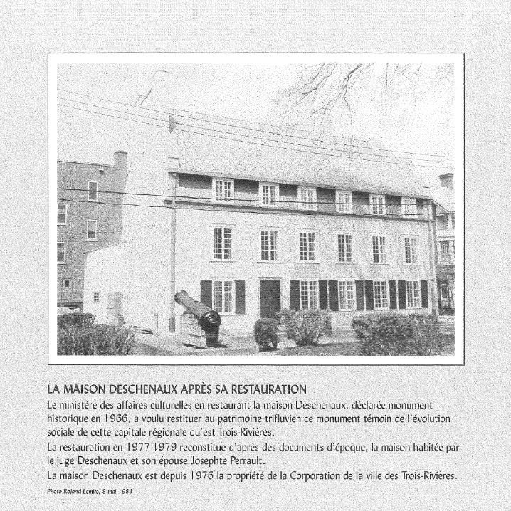 Une image en noir et blanc d'une maison de trois étages avec des fenêtres alignées, un canon ancien devant la maison, et des buissons devant. Il y a des lignes électriques au-dessus.
