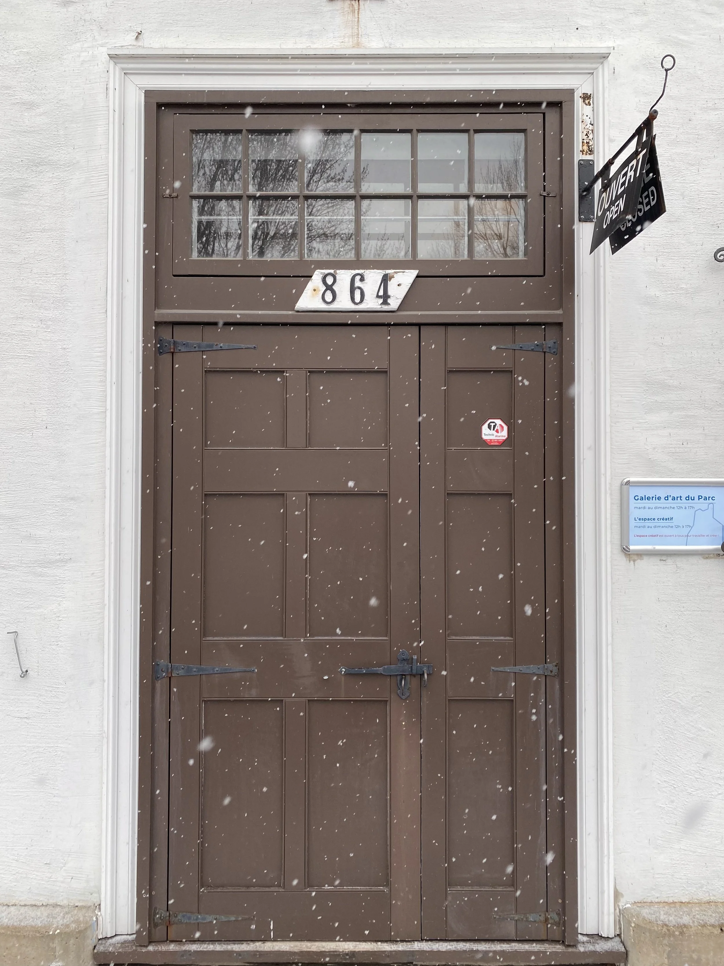 Porte en bois marron avec une fenêtre au sommet divisée en plusieurs petits carreaux. Numéro 864 affiché au-dessus. Signes d'une tempête de neige ou de glace sur la porte.