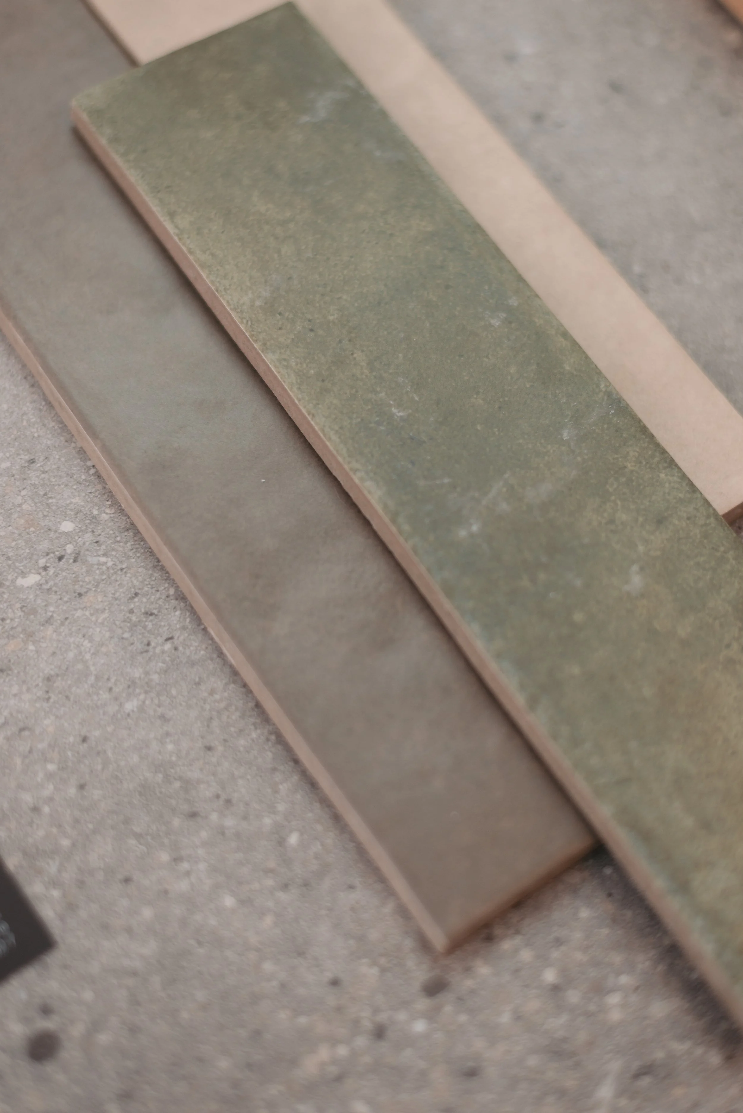 Close-up of three rectangular tiles with different earthy colors and textures on a rough concrete surface