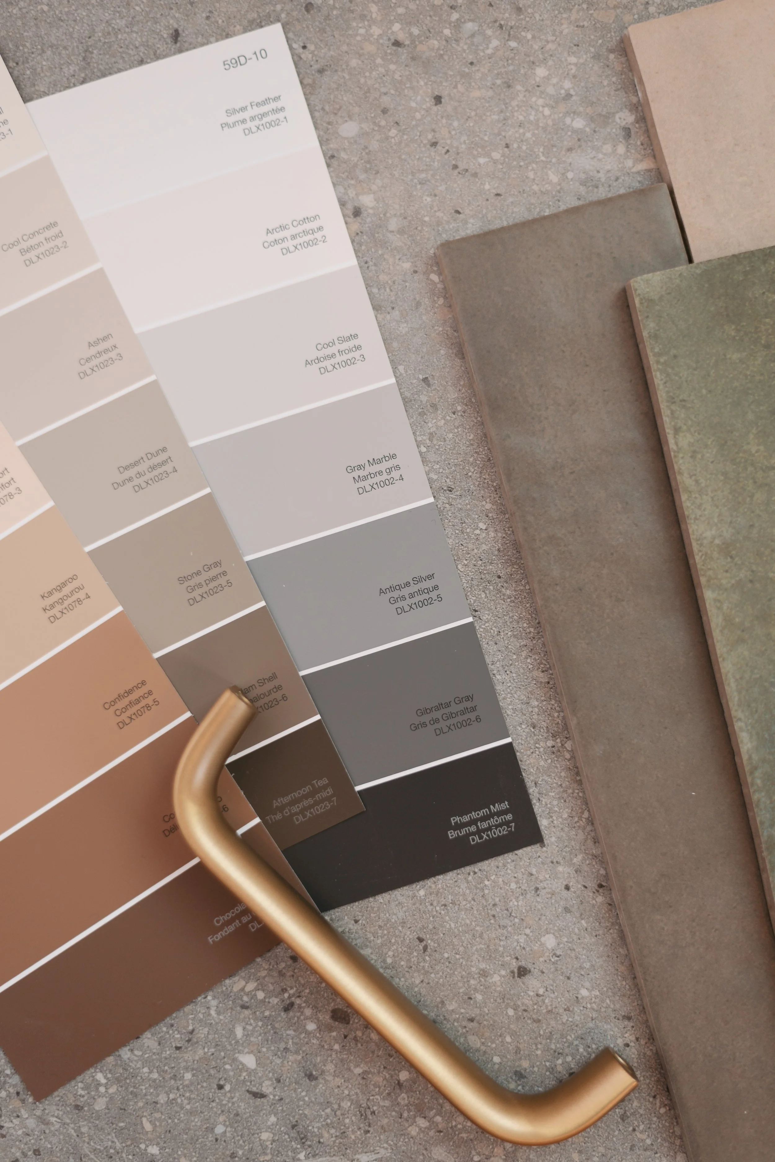 Color swatches, sample tiles, and a gold-colored handle on a concrete surface.