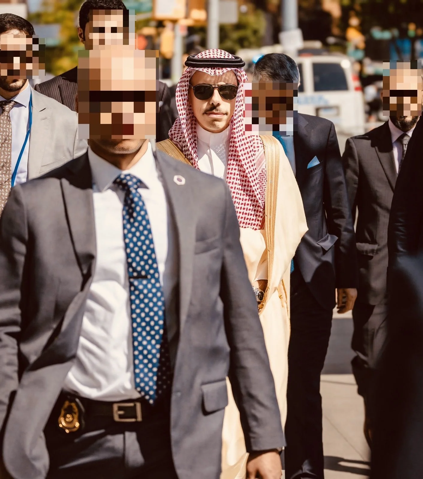 A group of men in formal suits, with one man in traditional Middle Eastern attire, walking outdoors.