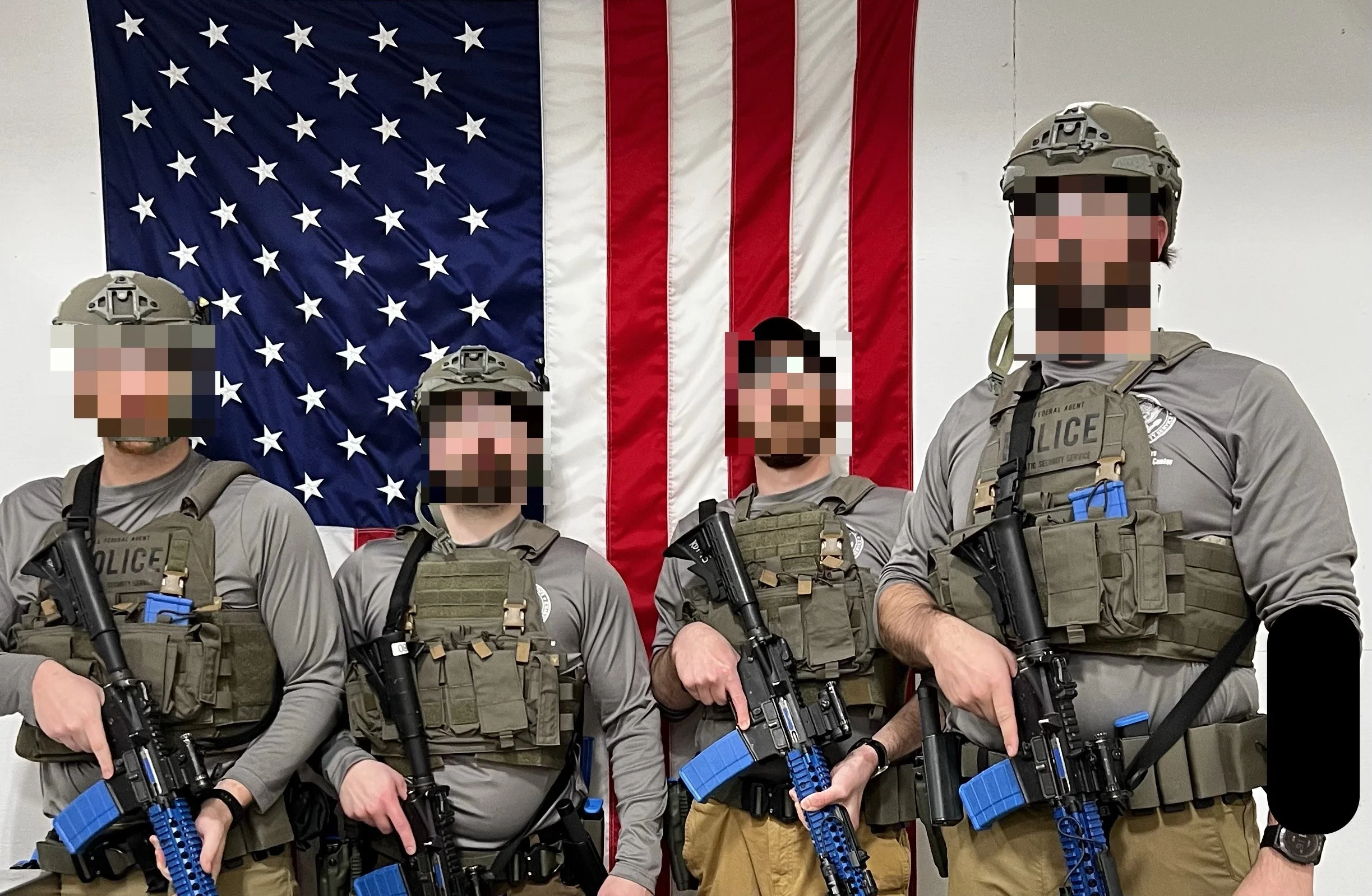 Four armed security personnel in tactical gear standing in front of an American flag.