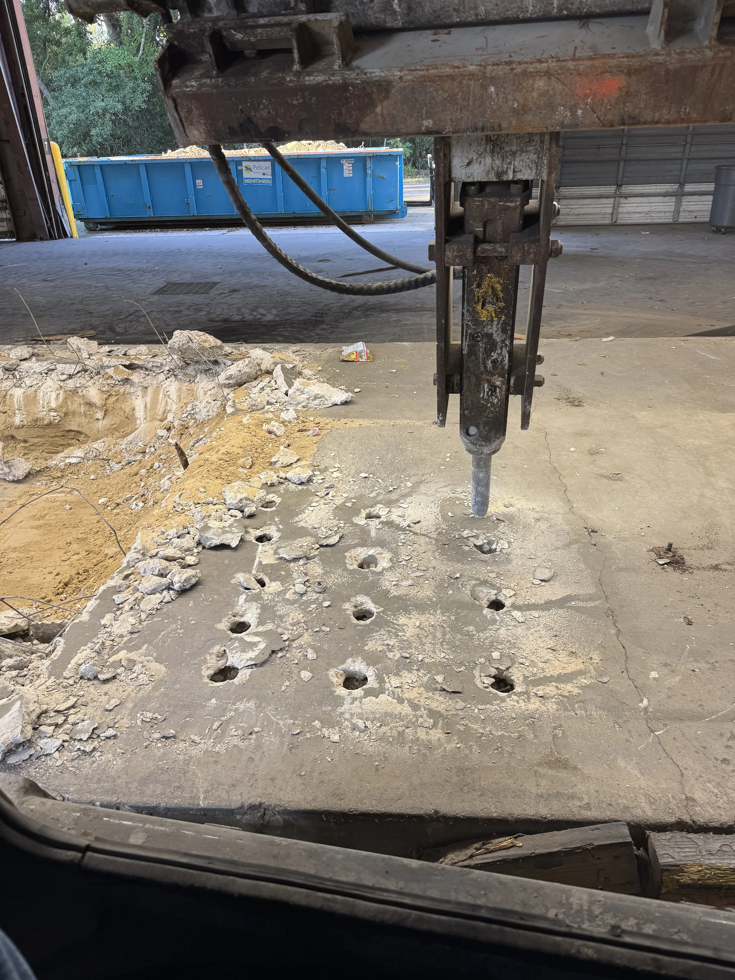  Hydraulic breaker attachment breaking through an interior warehouse concrete floor. 