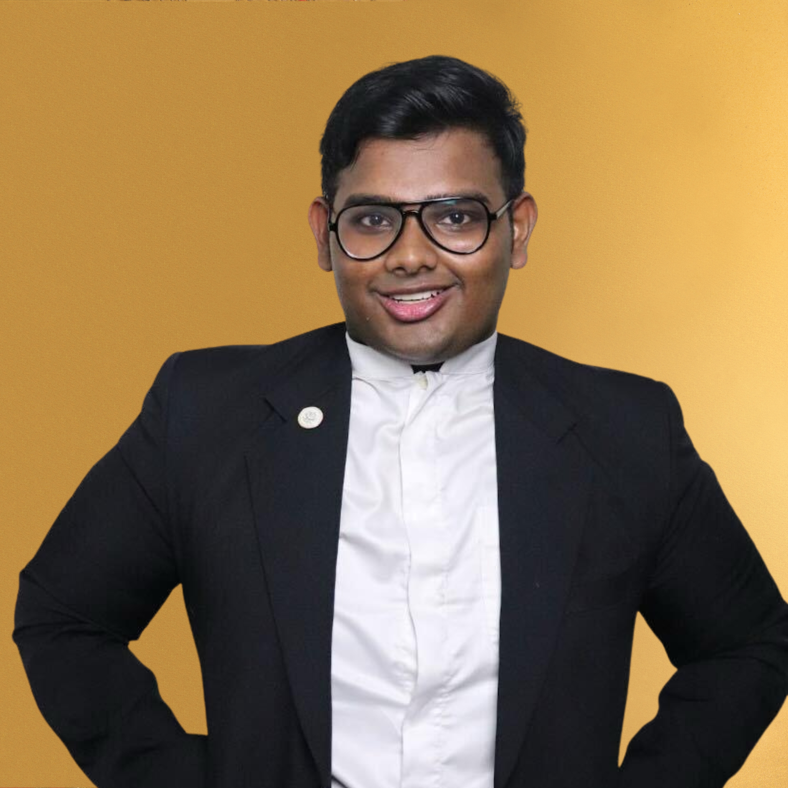 A young man in a black suit, white shirt, and glasses, smiling against a yellow background.