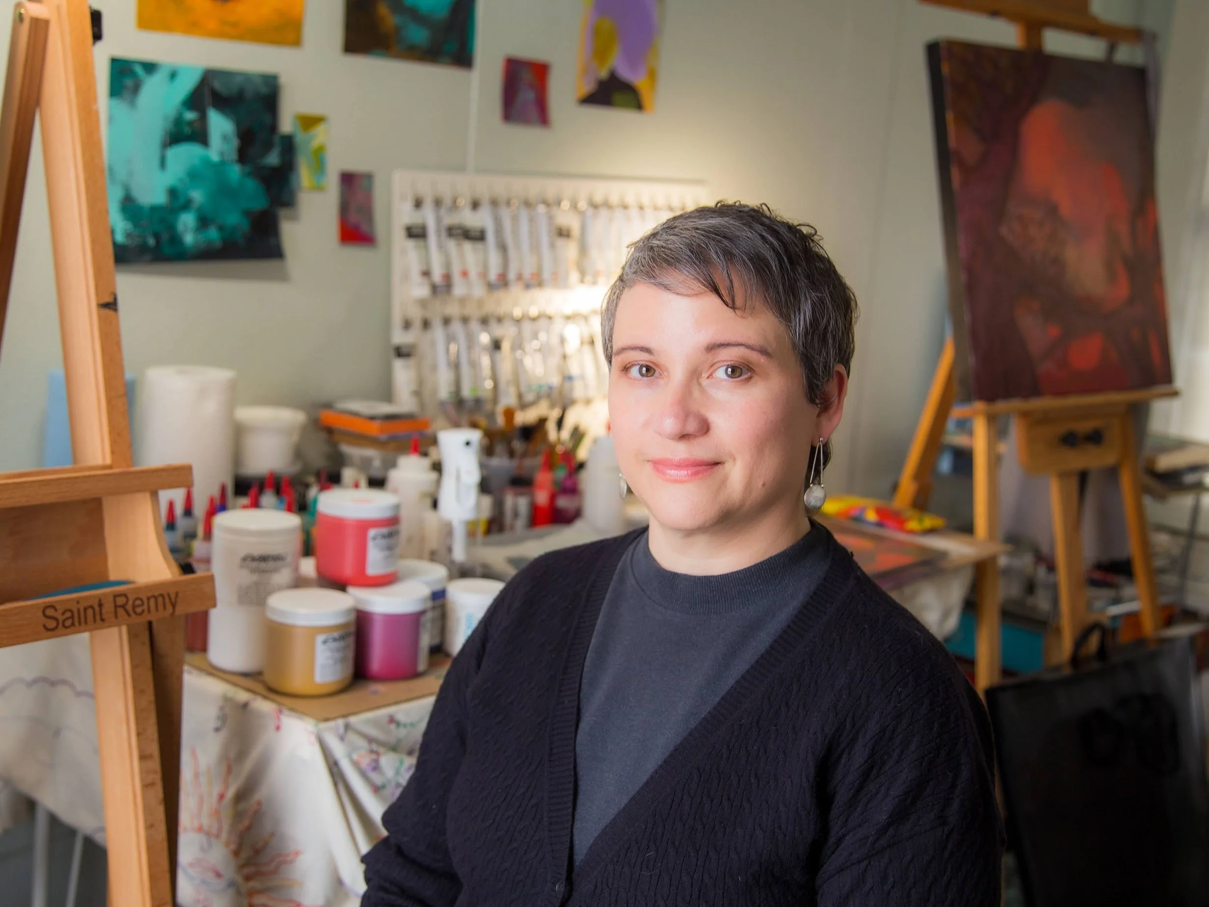 Artist in studio surrounded by paintings and art supplies