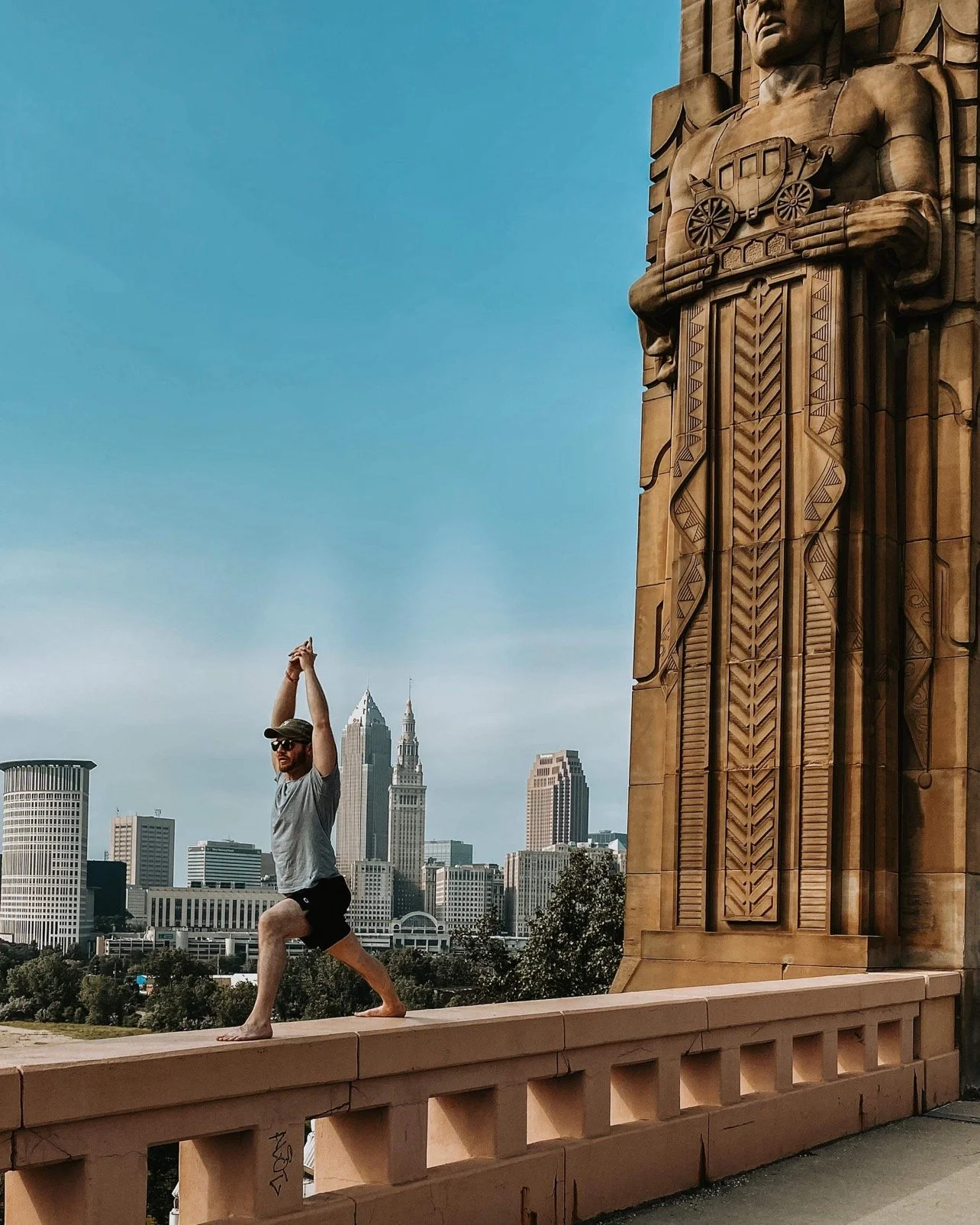 Steve Johnson practicing yoga beside a Cleveland bridge guardian with the city skyline behind him