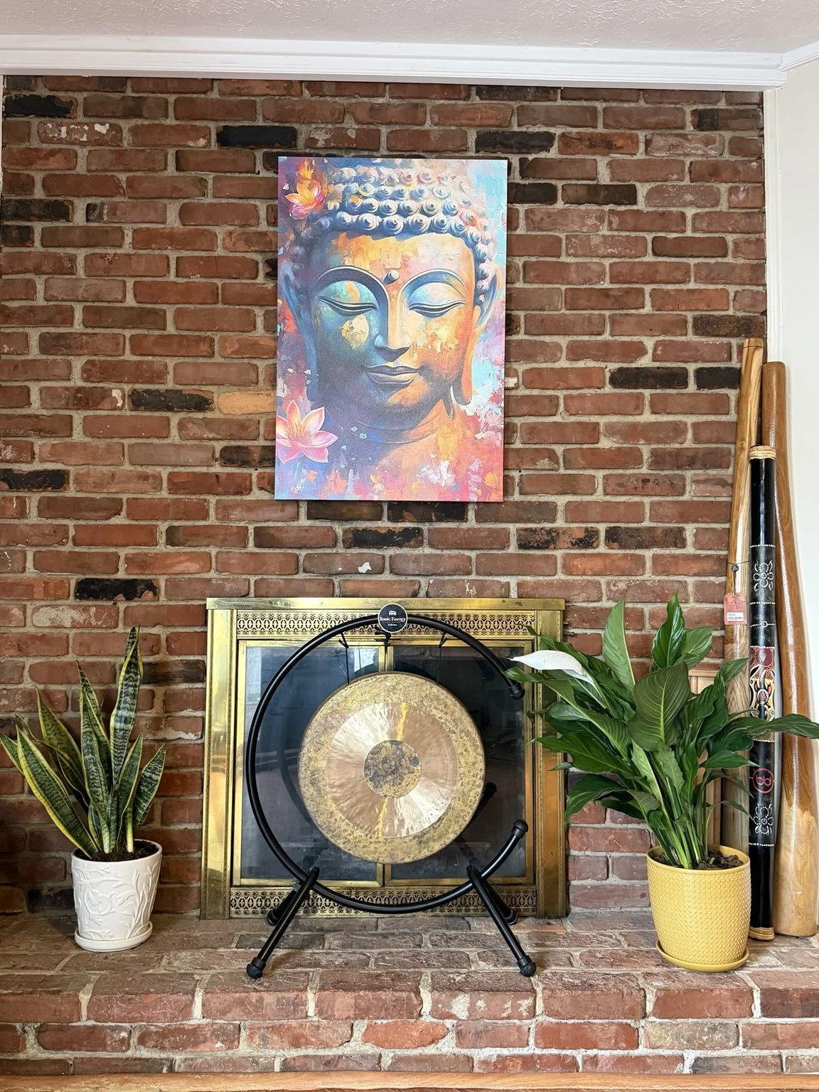 Gong, didgeridoos, plants, and Buddha artwork beside the brick fireplace at the Red Roots Yoga home studio in Mentor, Ohio.