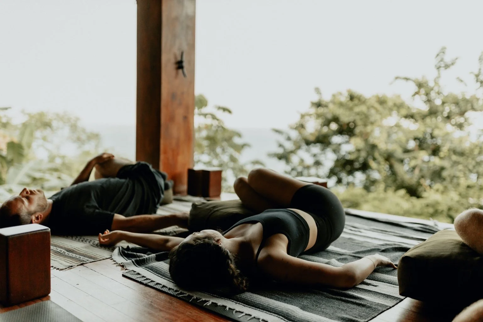 Students resting in gentle supported yoga poses in a warm, sunlit practice space