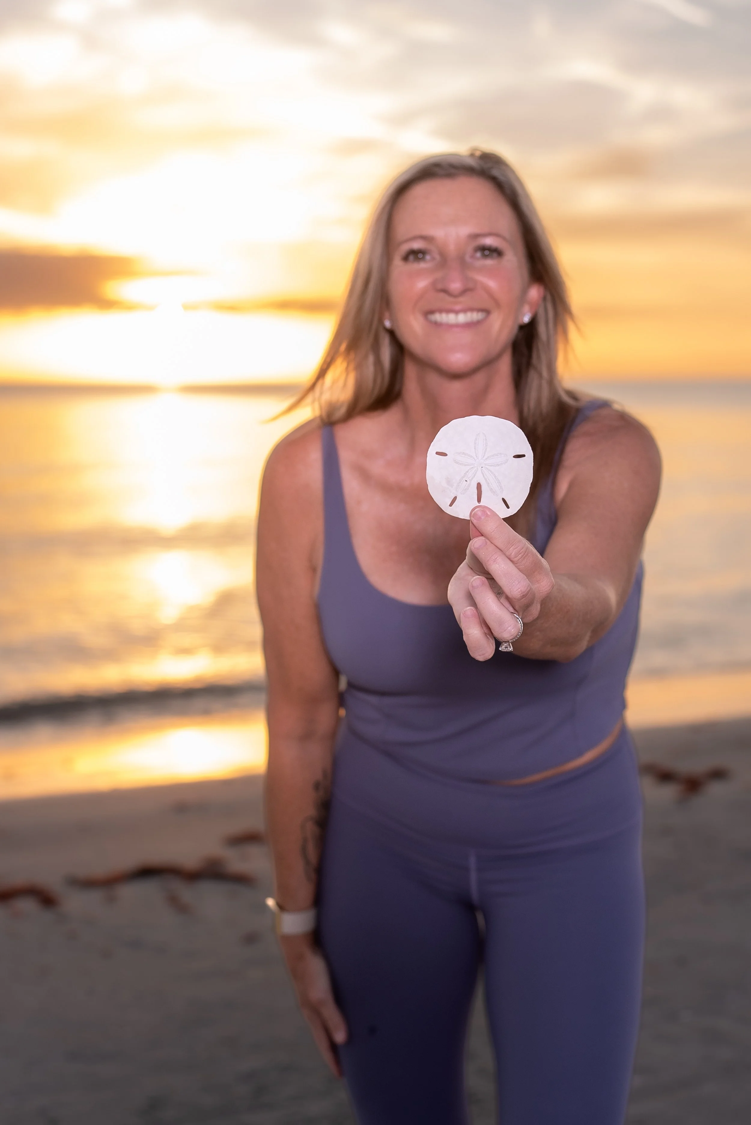 Monica Leonard holding a sand dollar on the beach at sunset