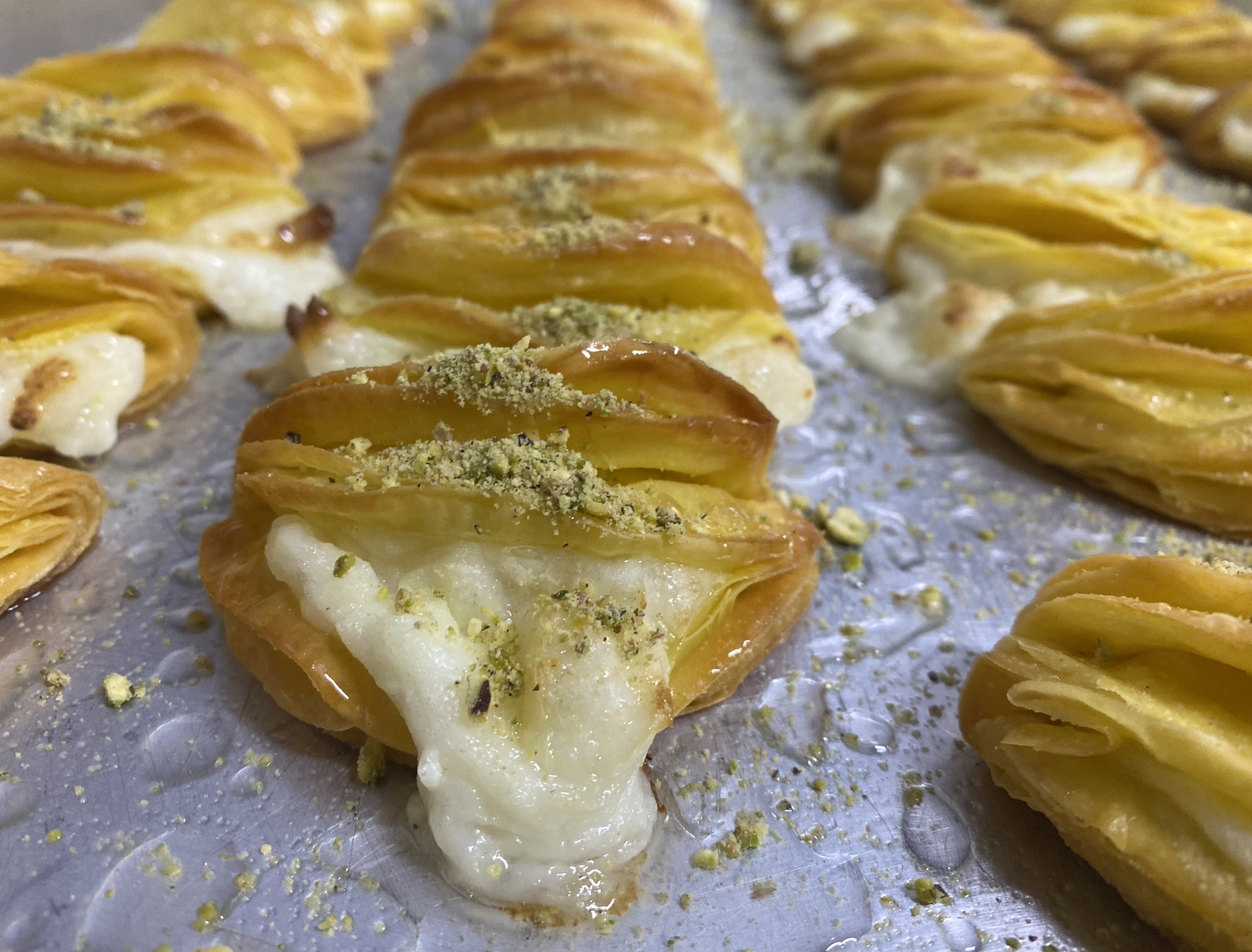 Close-up of baked baklava with layers of flaked pastry, honey glaze, and crushed pistachios on top.