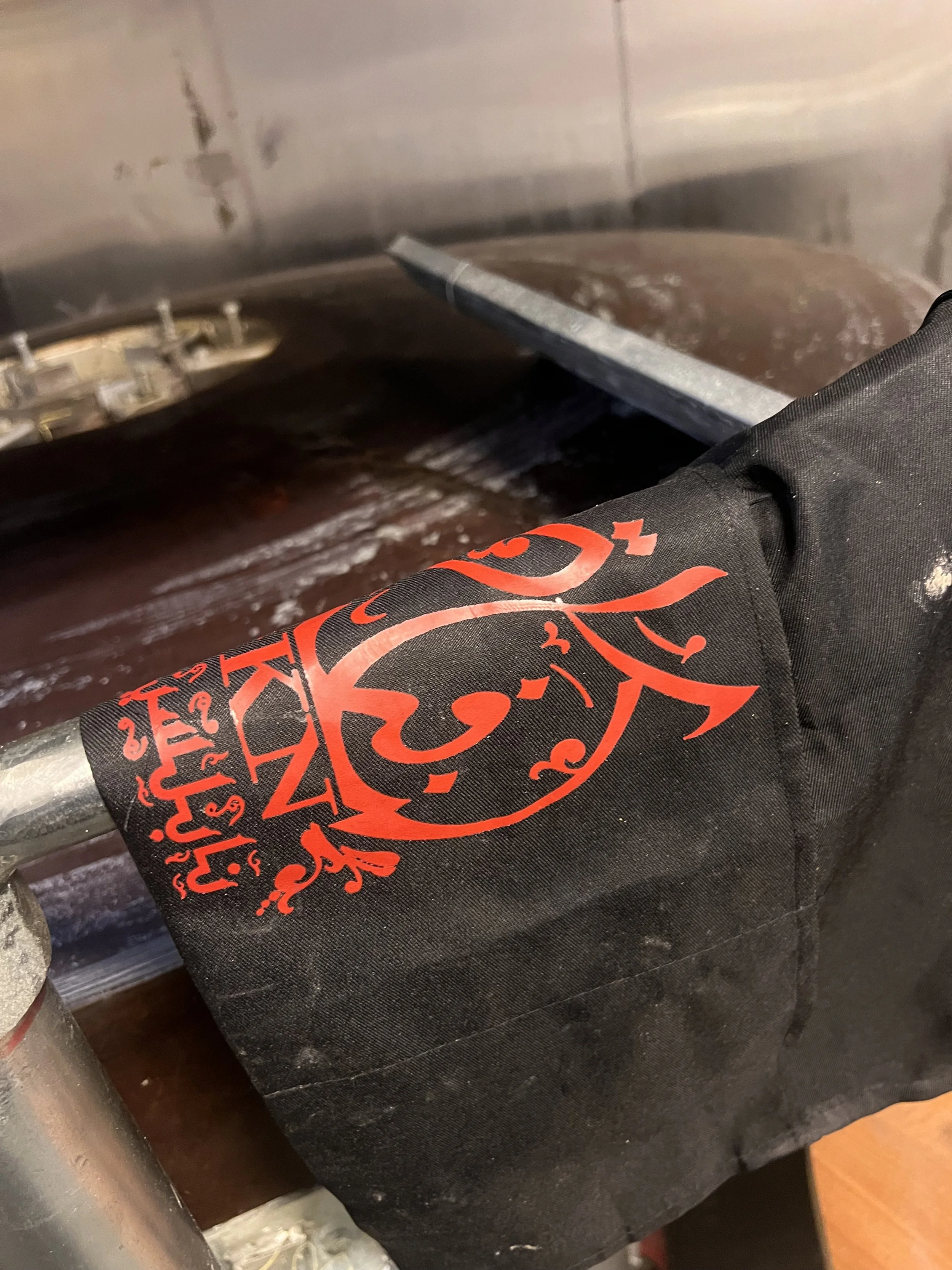 Close-up of a black cloth or bag with a red ornate design or logo, resting on a dark surface near a metal object.