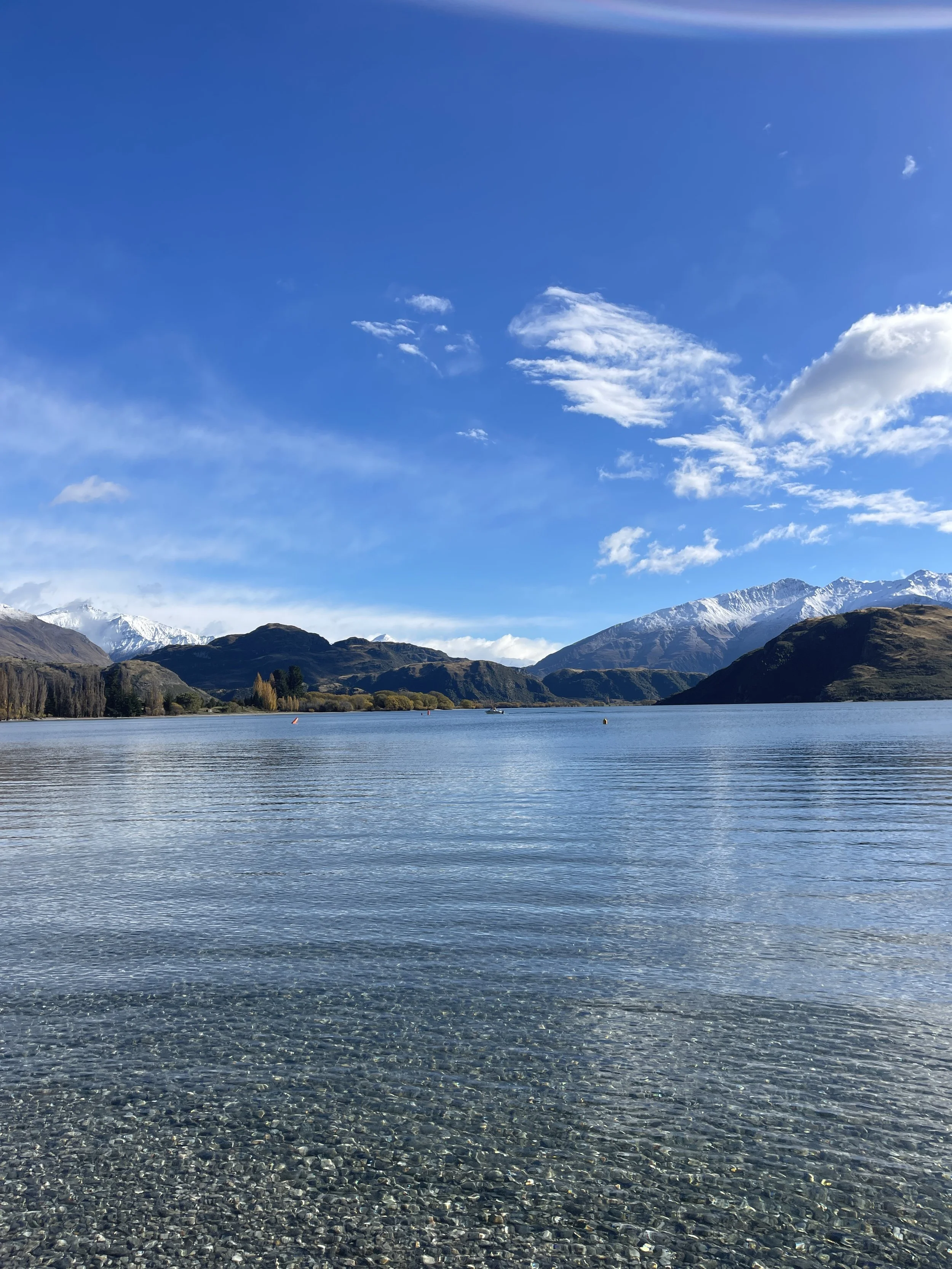 Scenic view of a lake surrounded by mountains with snow-capped peaks under a blue sky with clouds.