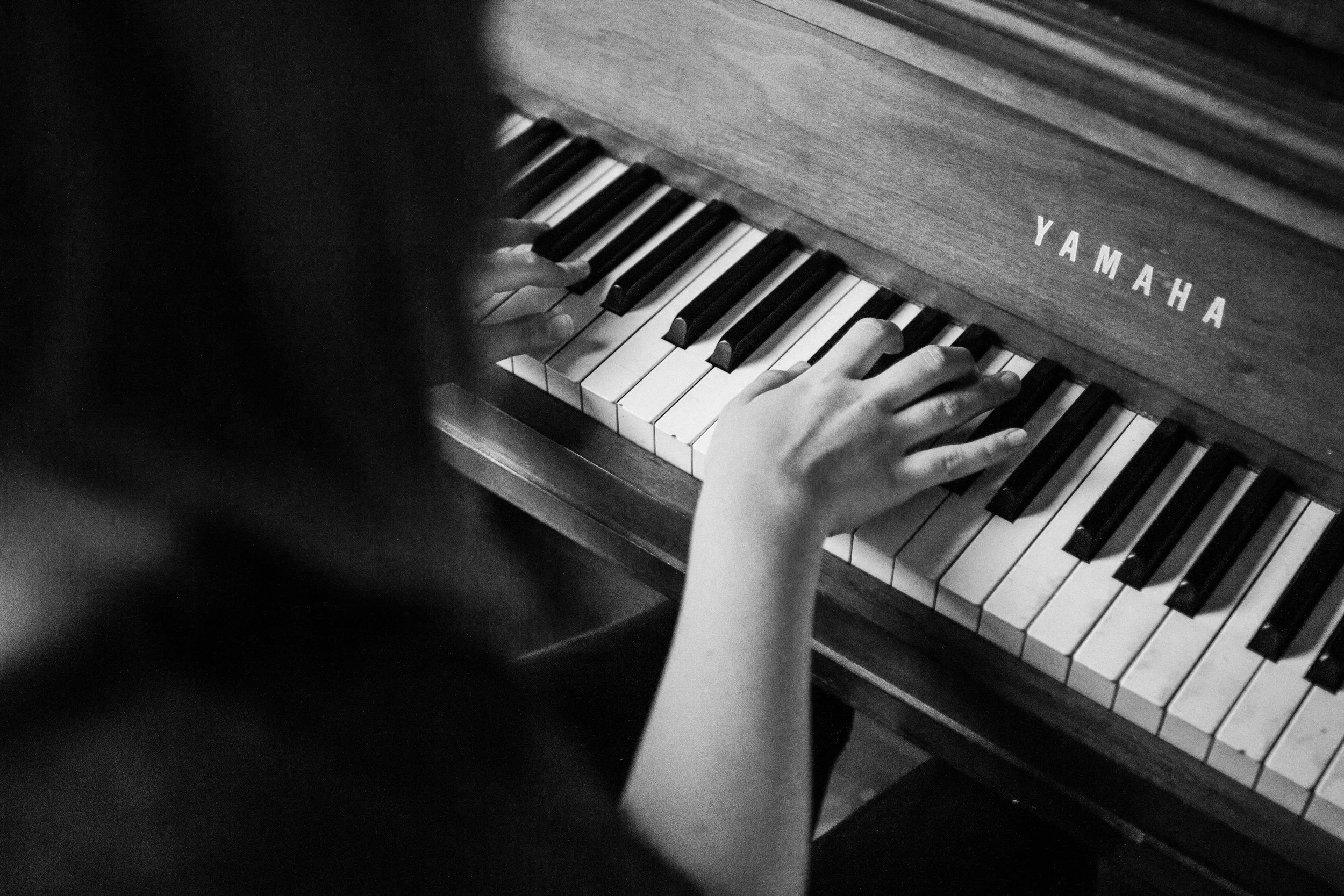 Child playing a Yamaha upright piano with hands on the keys.
