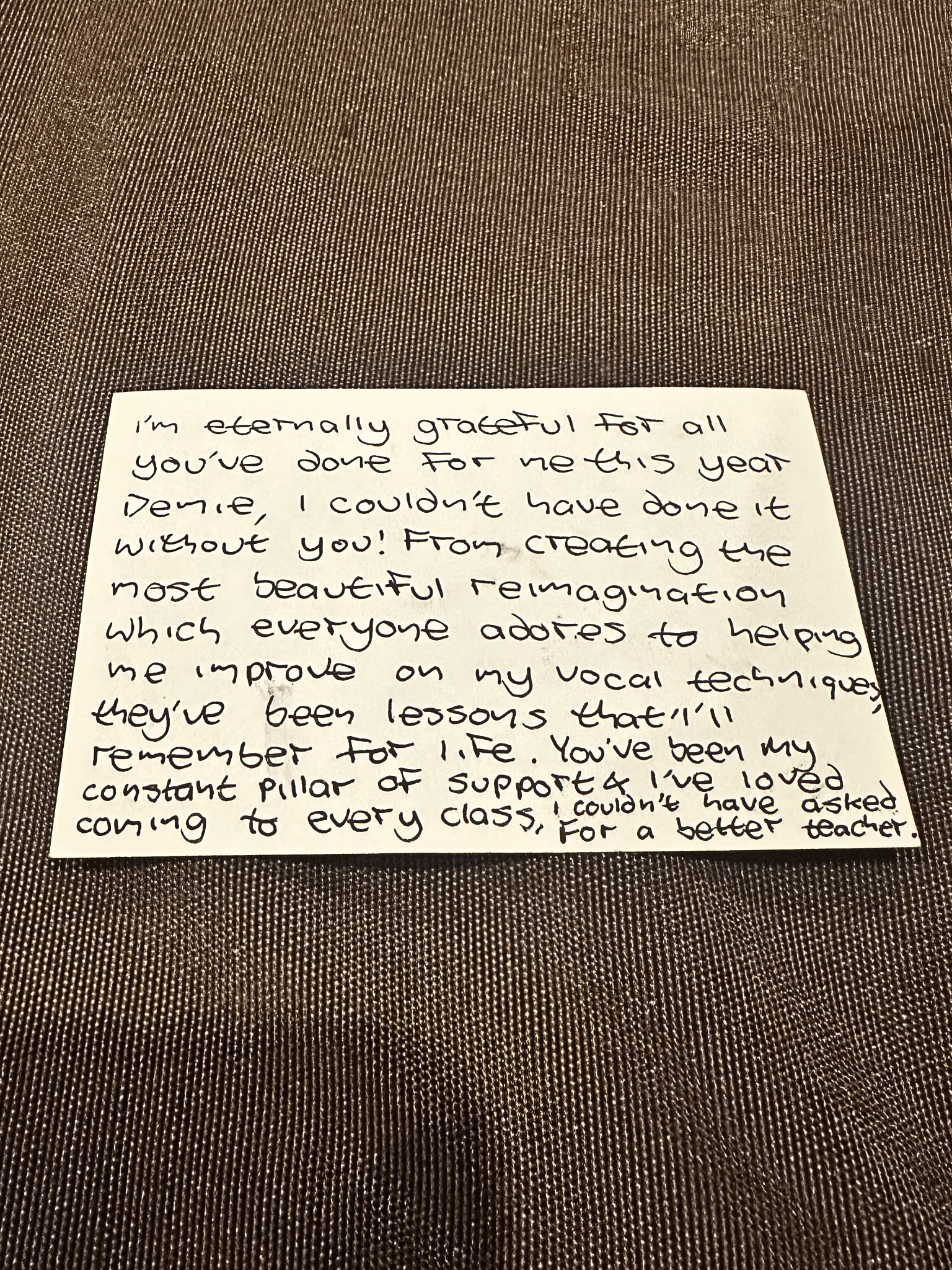 A handwritten note on a piece of paper placed on a textured fabric surface, expressing gratitude for support and inspiration.