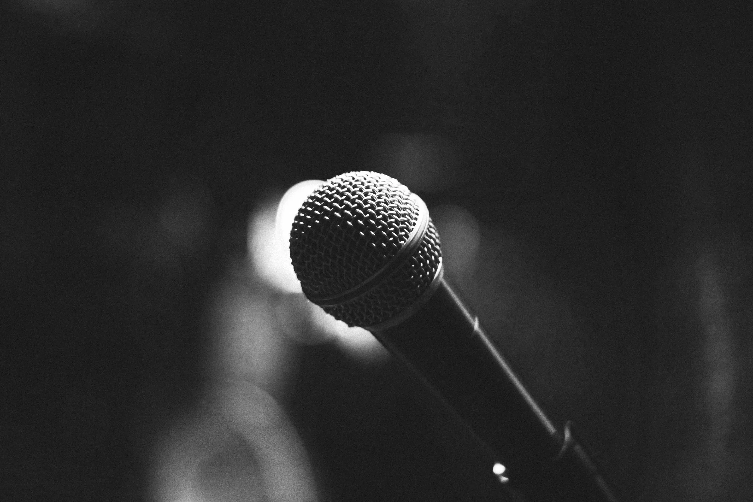 A black-and-white photo of a microphone on a stand, with blurred lights in the background promoting singing lessons.
