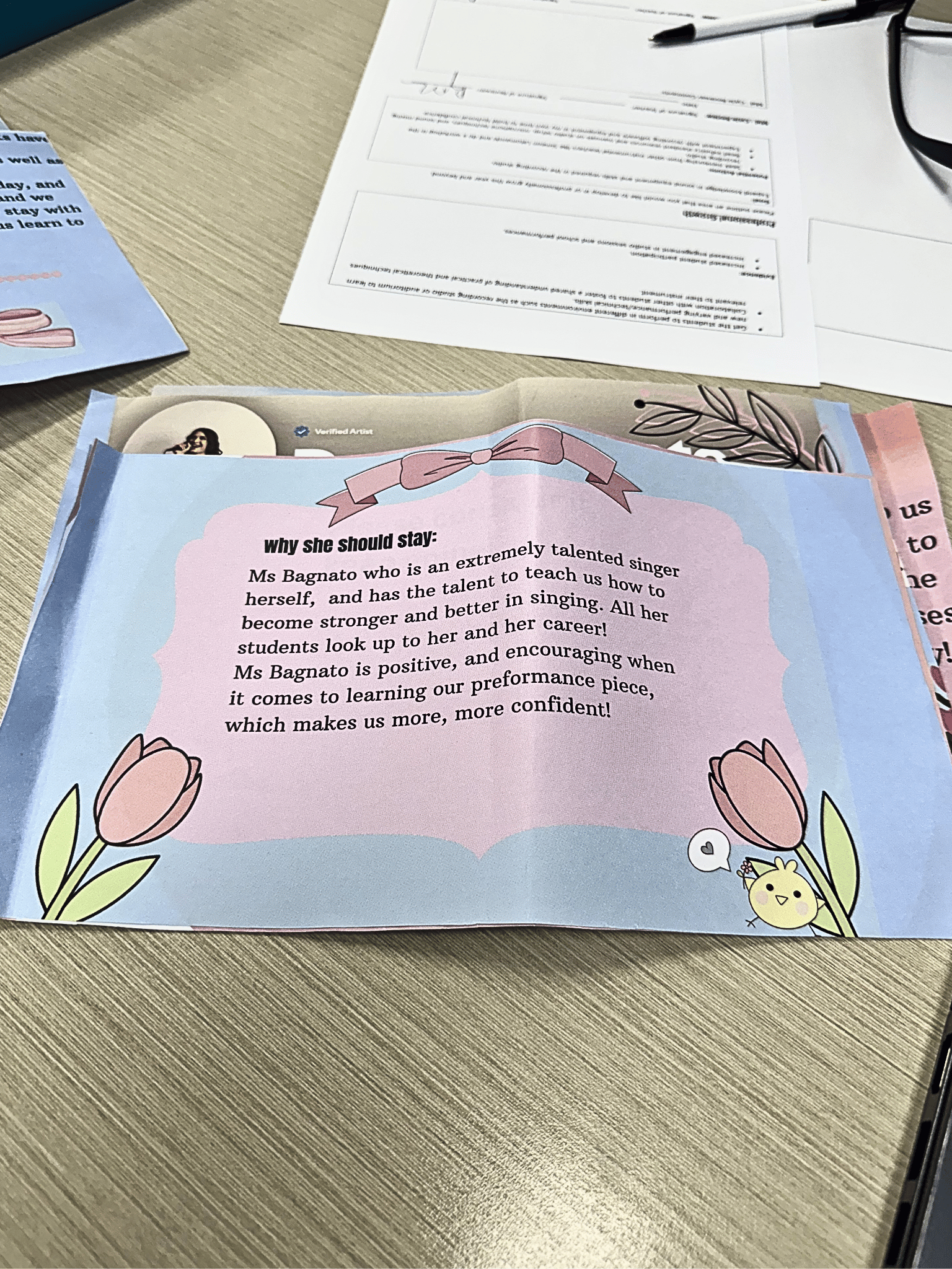 A colorful flyer with flowers and a cute bird illustration. The flyer has a pink and blue background with text about Ms. Bagnato and her students' progress in singing.