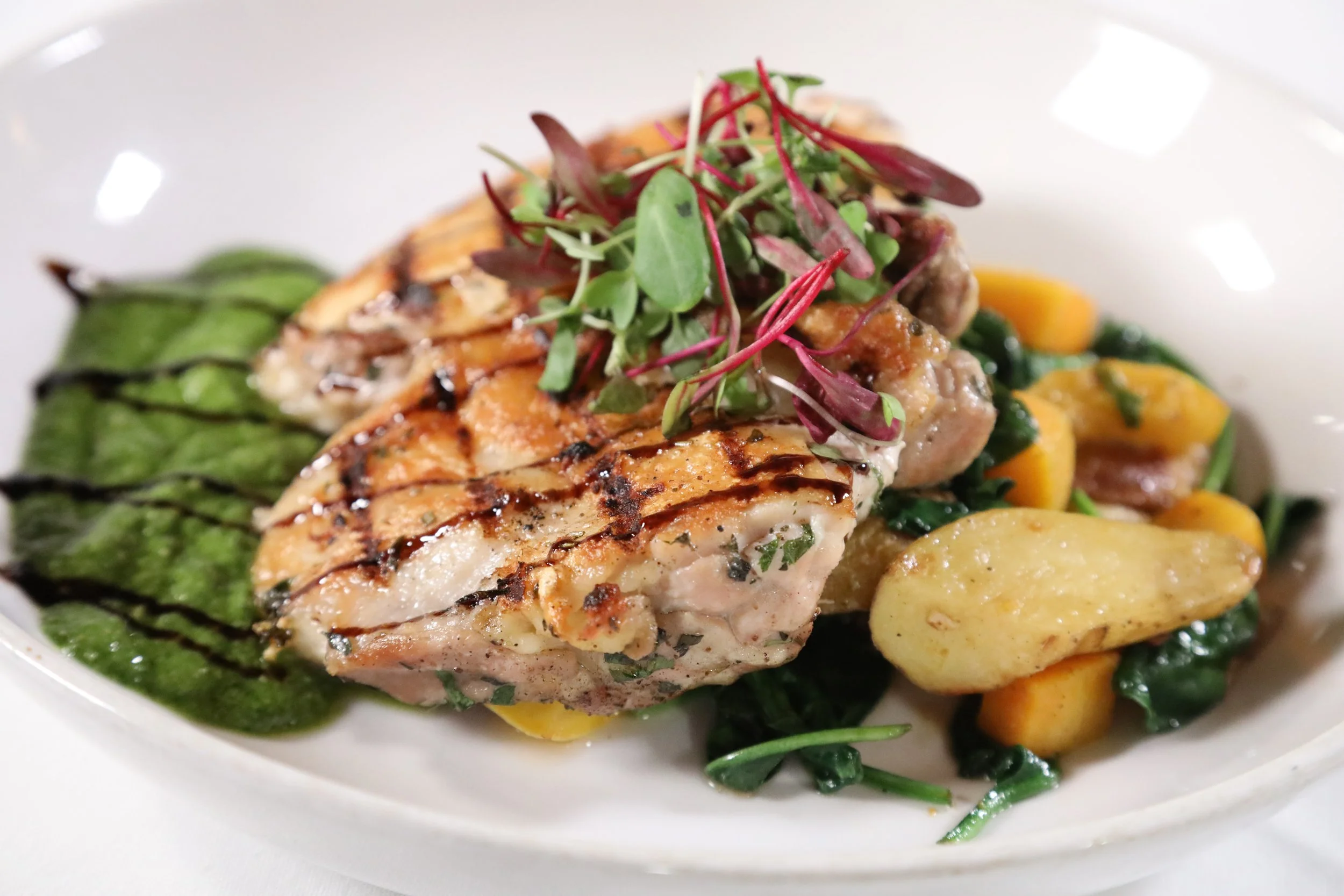 Grilled salmon fillet garnished with microgreens, served with roasted potatoes, sautéed greens, and roasted squash.