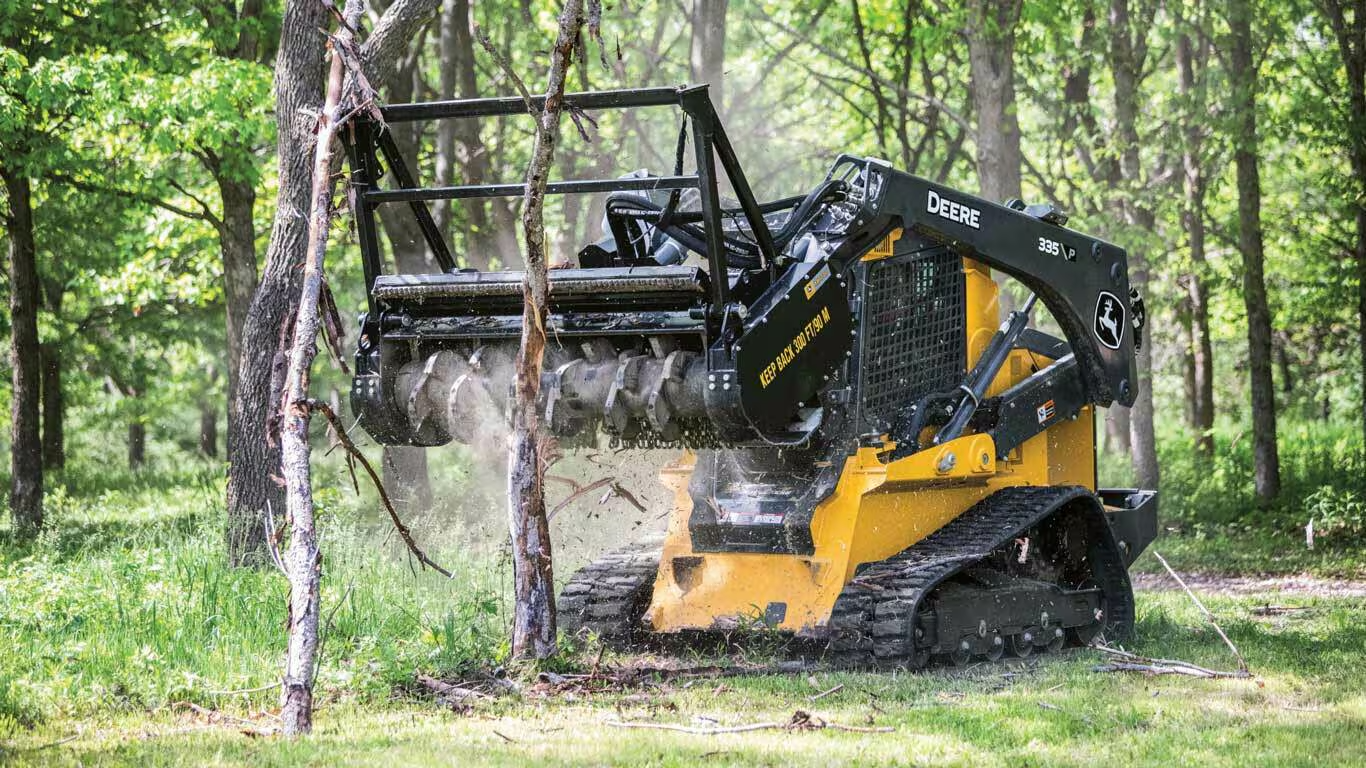 John Deere compact track loader with forestry mulching head clearing brush in a wooded area in Southern Illinois.