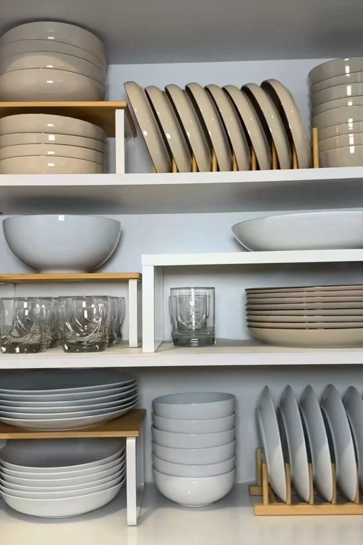 Kitchen shelves filled with neatly stacked white bowls, plates, and glassware.
