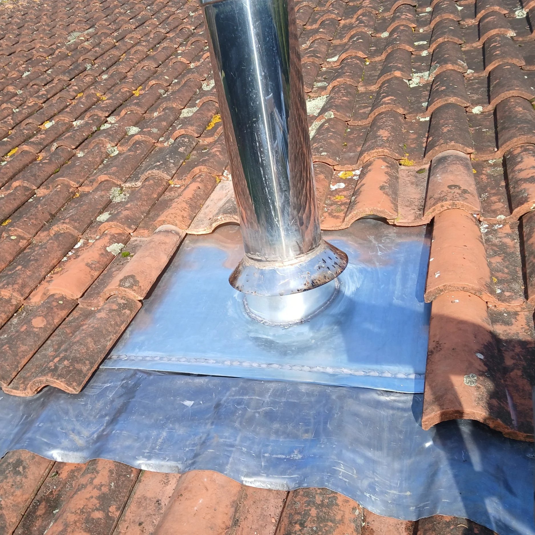 Installation d'une cheminée en métal sur un toit en tuiles, avec un revêtement en métal autour de la sortie de cheminée.