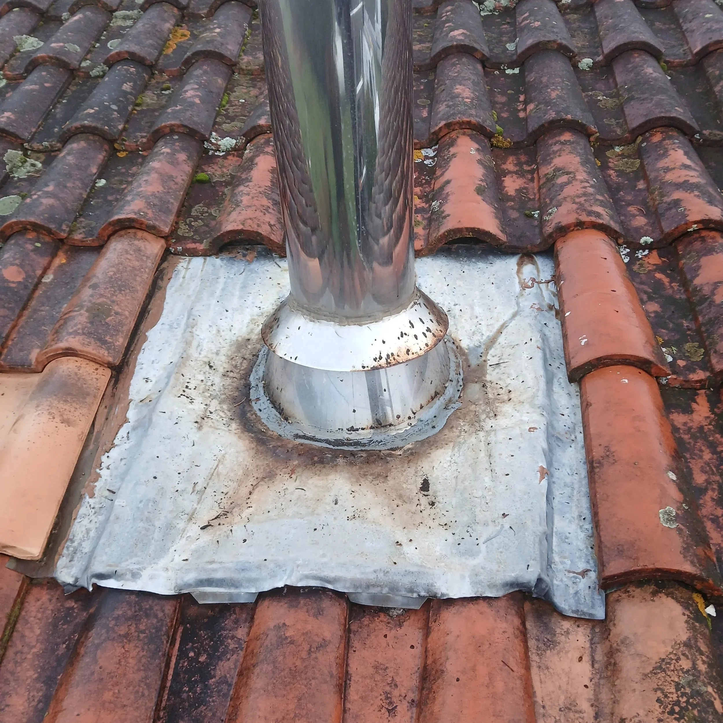 Cloison en métal brillant autour d'une cheminée de toit en tuiles rouges et noires.