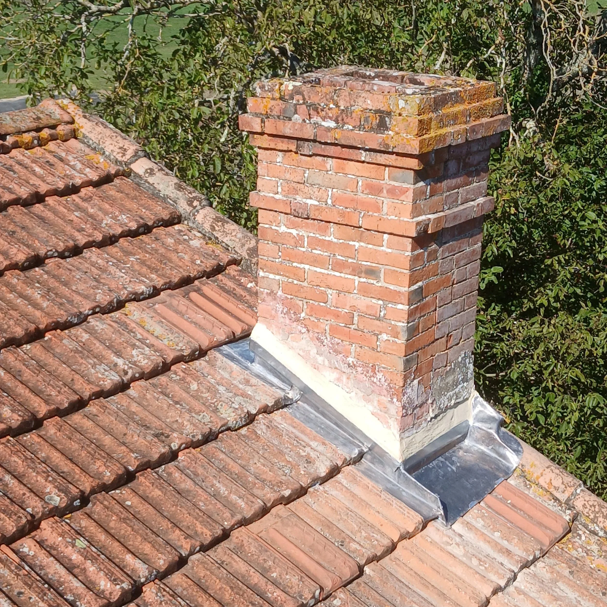 Cheminée en briques rouges sur le toit d'une maison avec des tuiles en terre cuite.