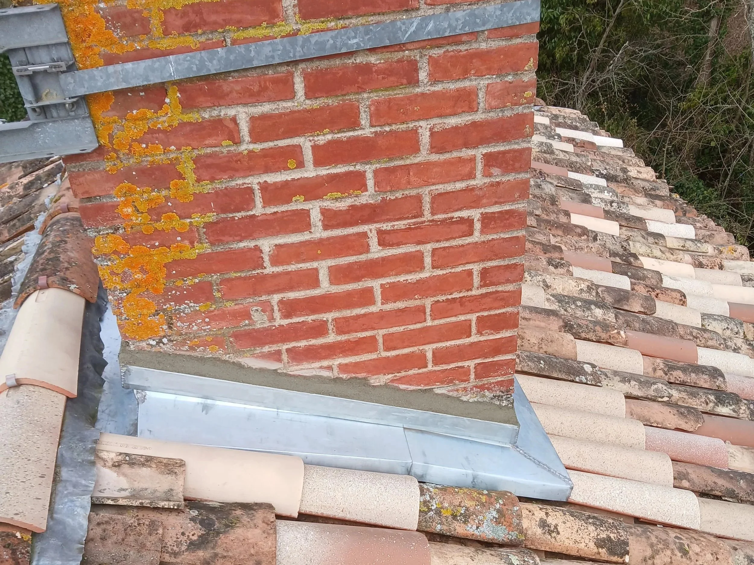 Une cheminée en briques rouges sur un toit en tuiles, avec de la mousse et des lichens jaunes sur la surface.