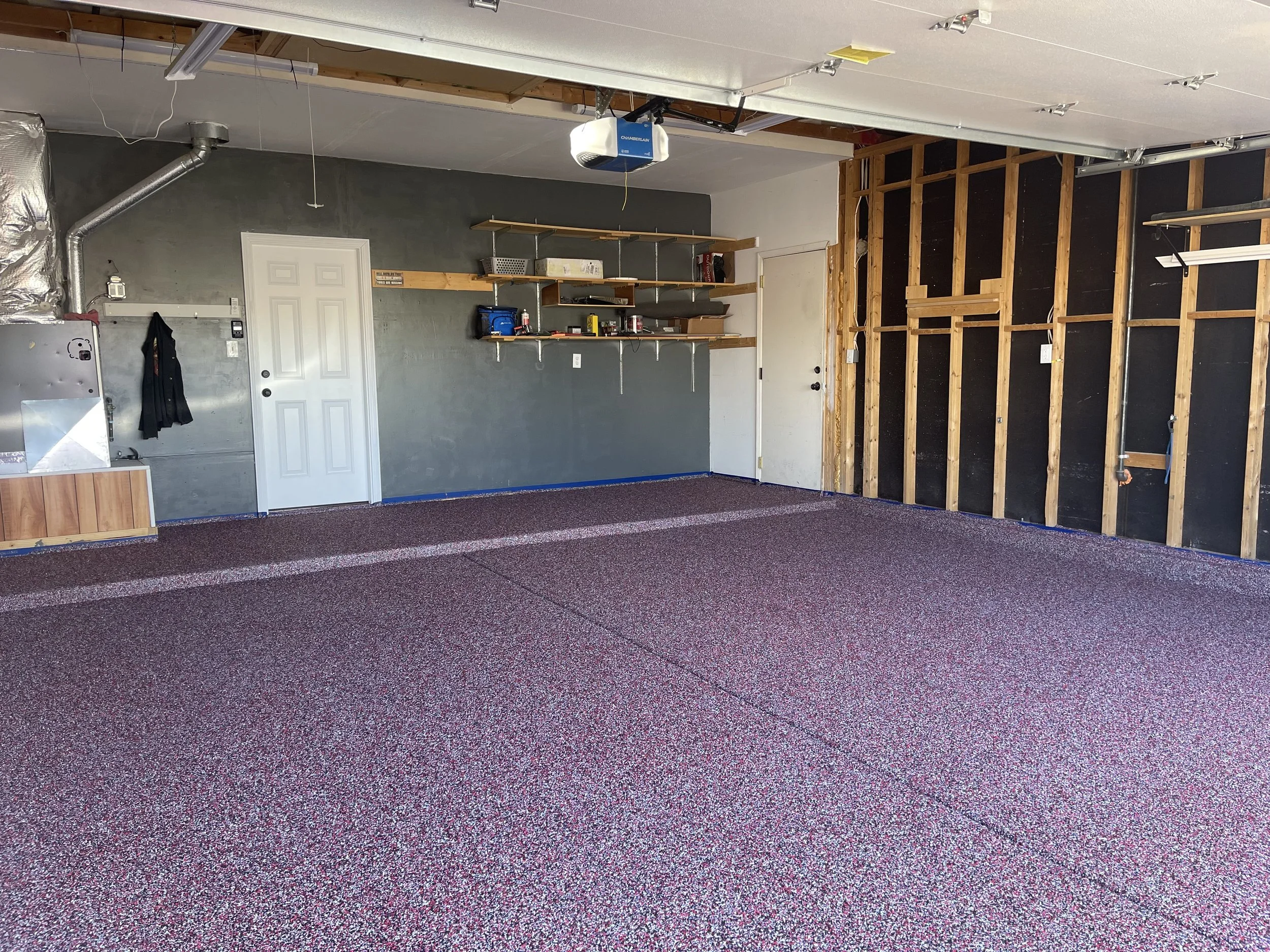 Empty garage with unfinished wall, shelves, a door, and a red-speckled epoxy floor.