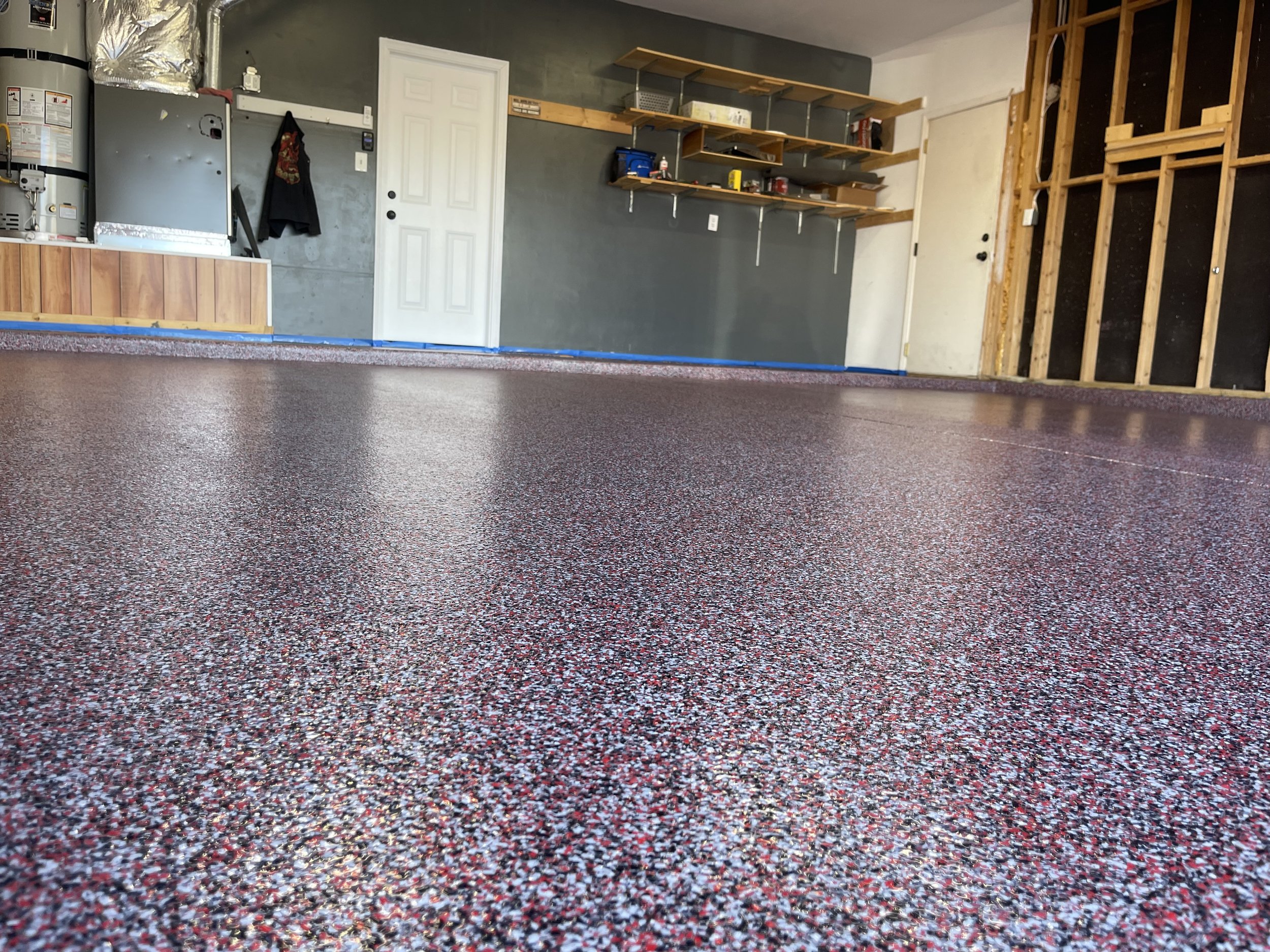Empty garage with a speckled red, white, and black epoxy floor, a water heater, and shelves on the wall.