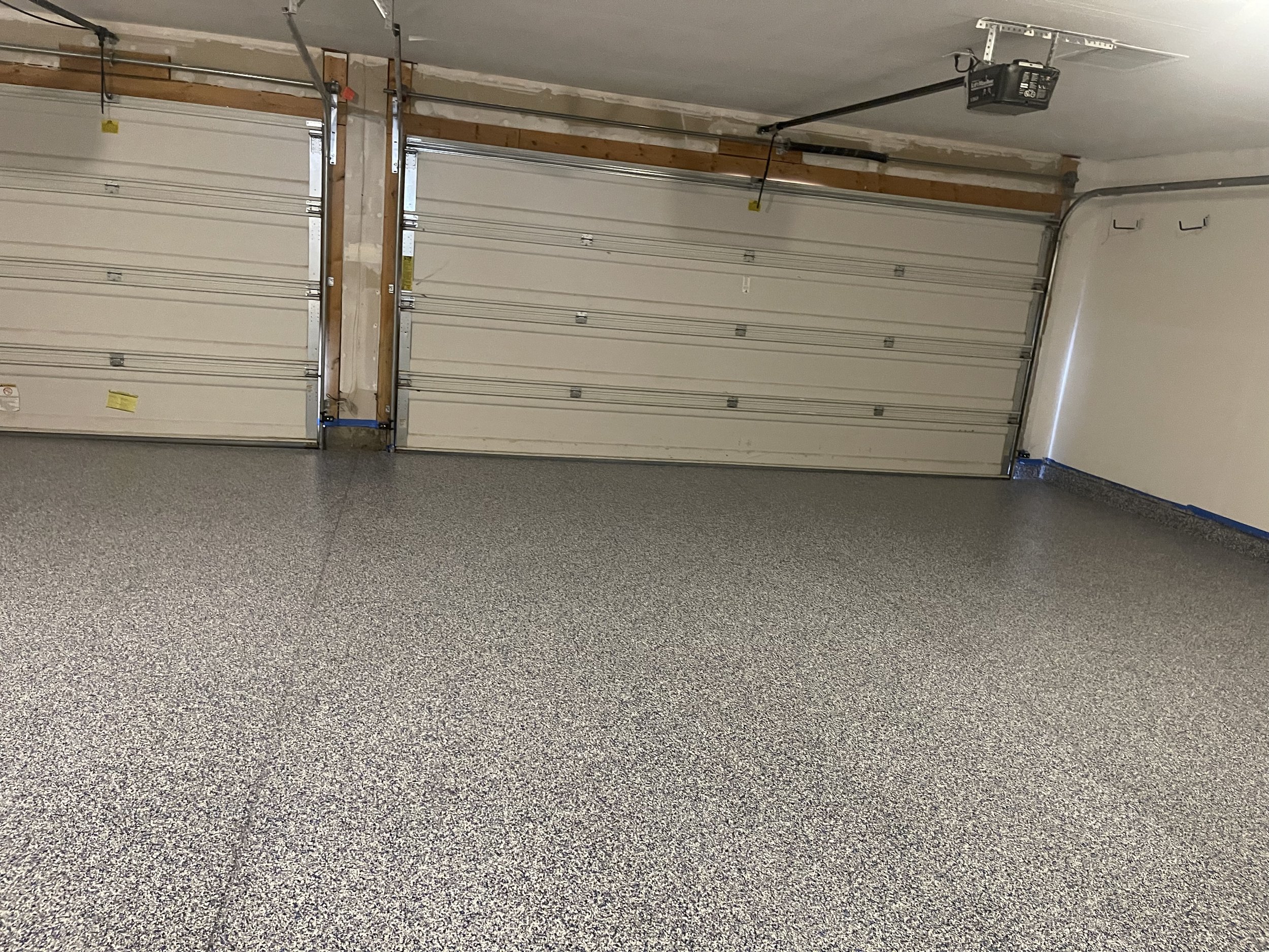 Empty, clean two-car garage with speckled gray epoxy floor, white walls, and closed white garage doors.