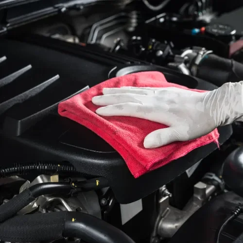 A person wearing white gloves cleaning a car engine with a red cloth.