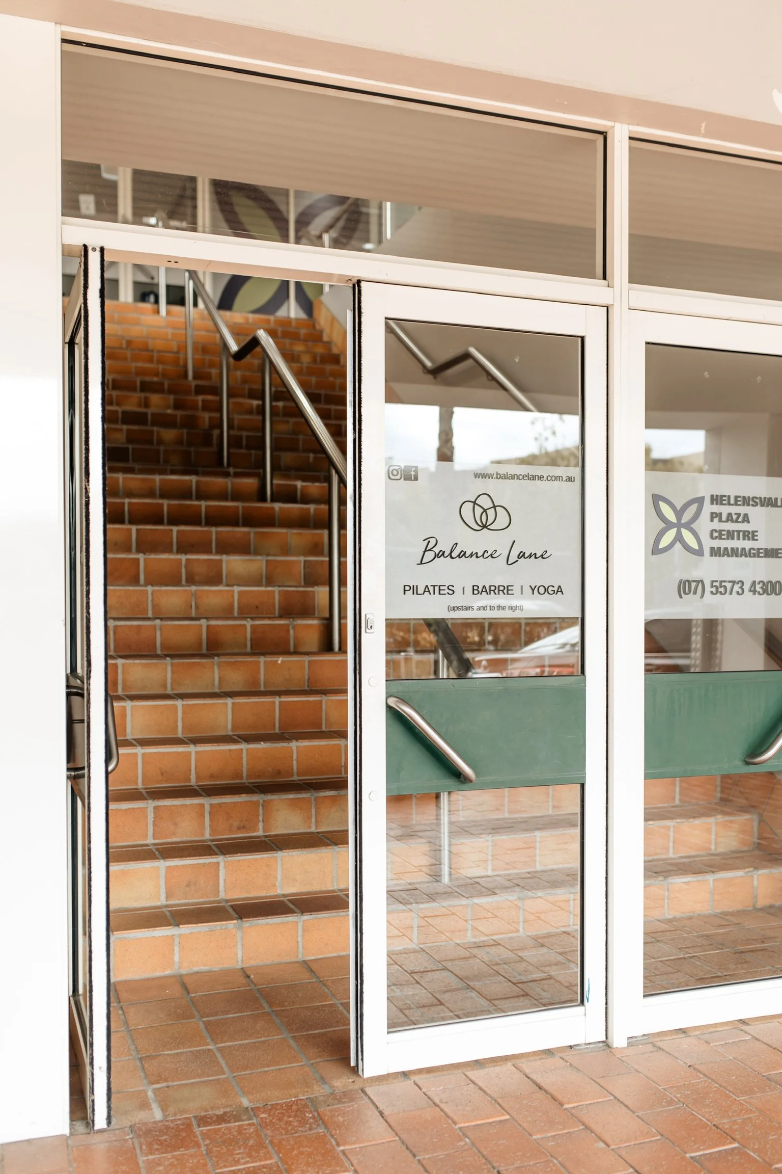 Entrance to a fitness center with glass doors showing a staircase with brick steps inside.