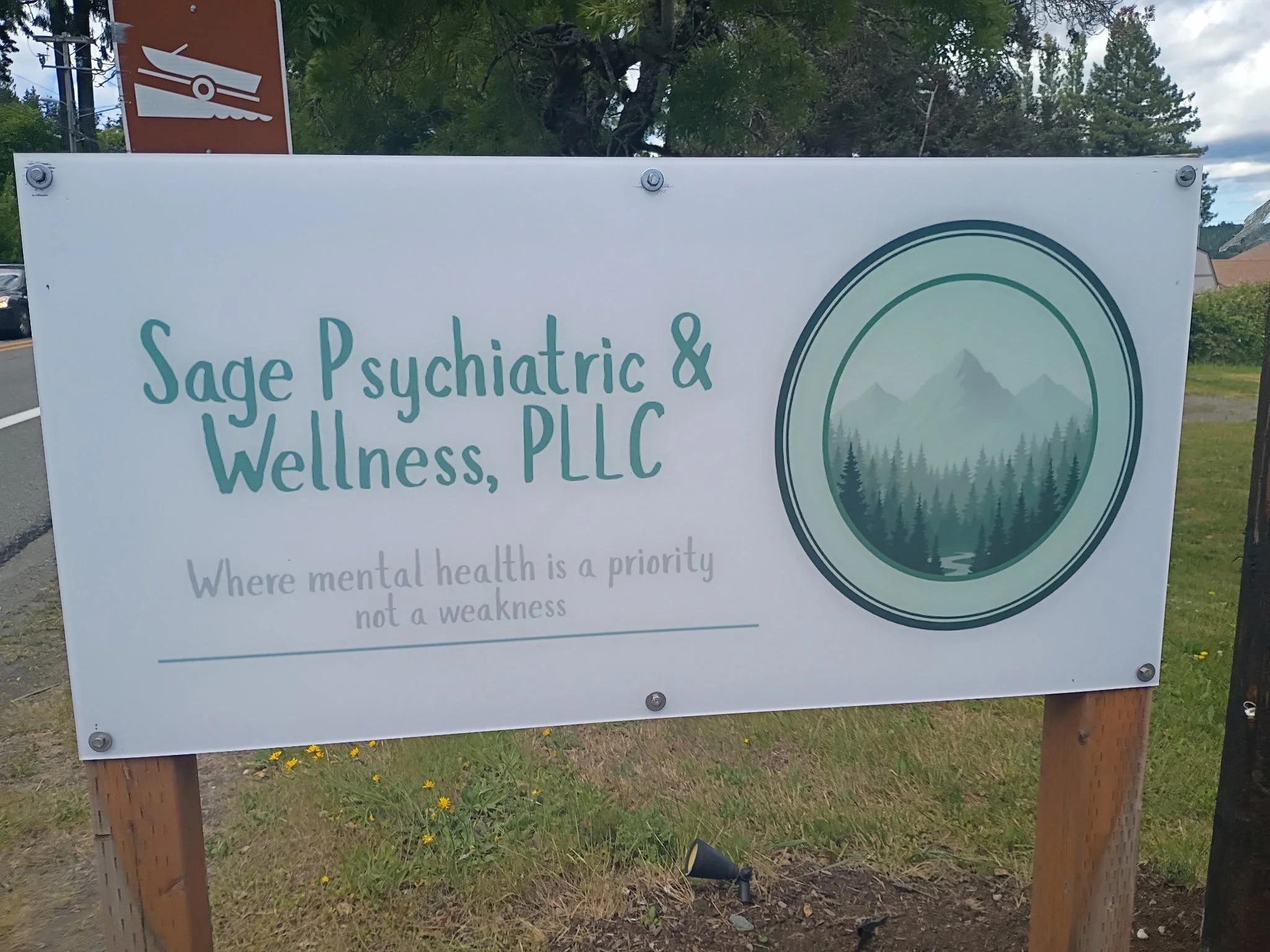 Signboard for Sage Psychiatric & Wellness PLLC with mountain and forest logo, outdoor setting with trees and cloudy sky.