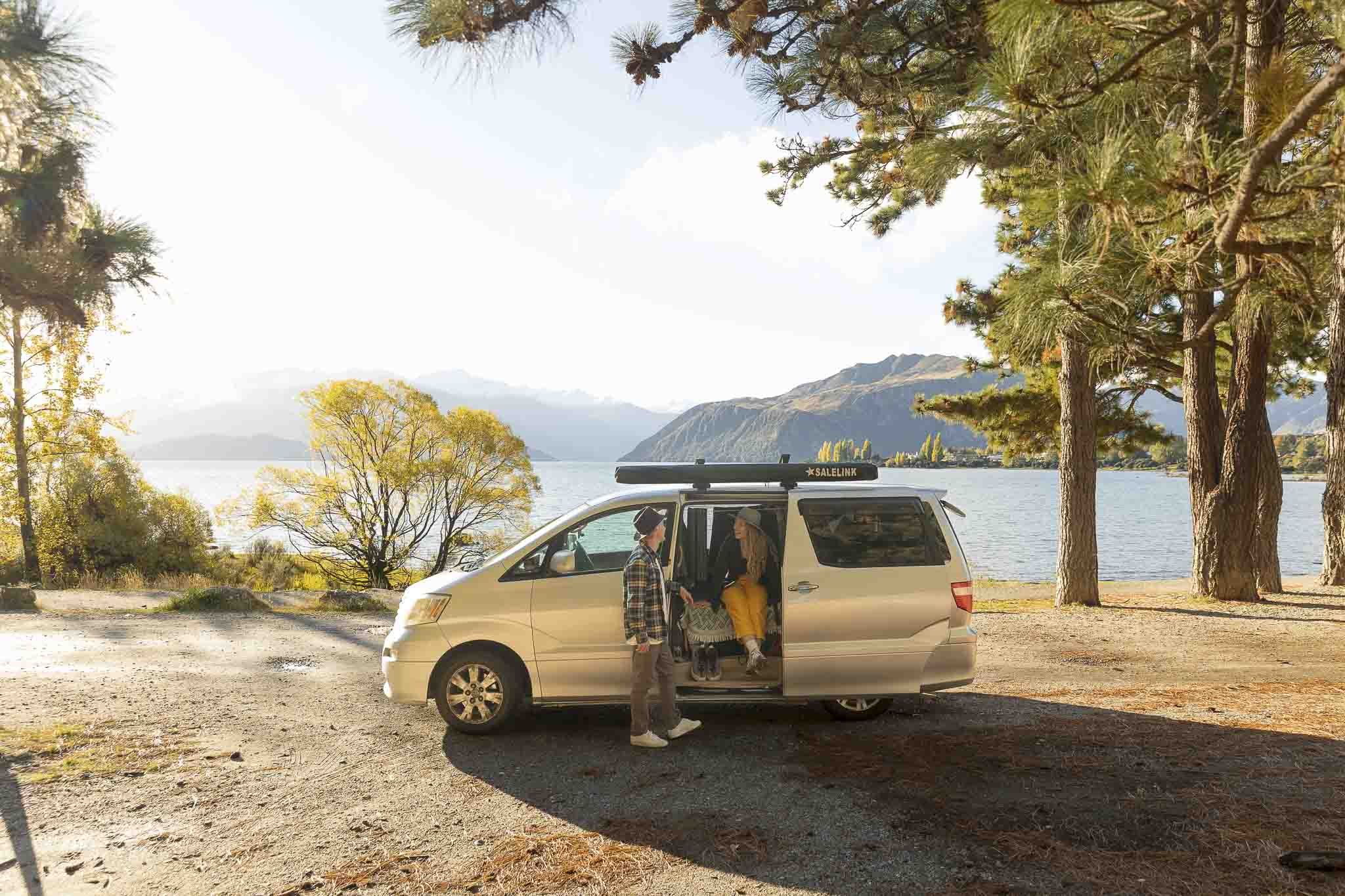 Couple sitting in their van in front of lake wanaka and the surrounding mountains
