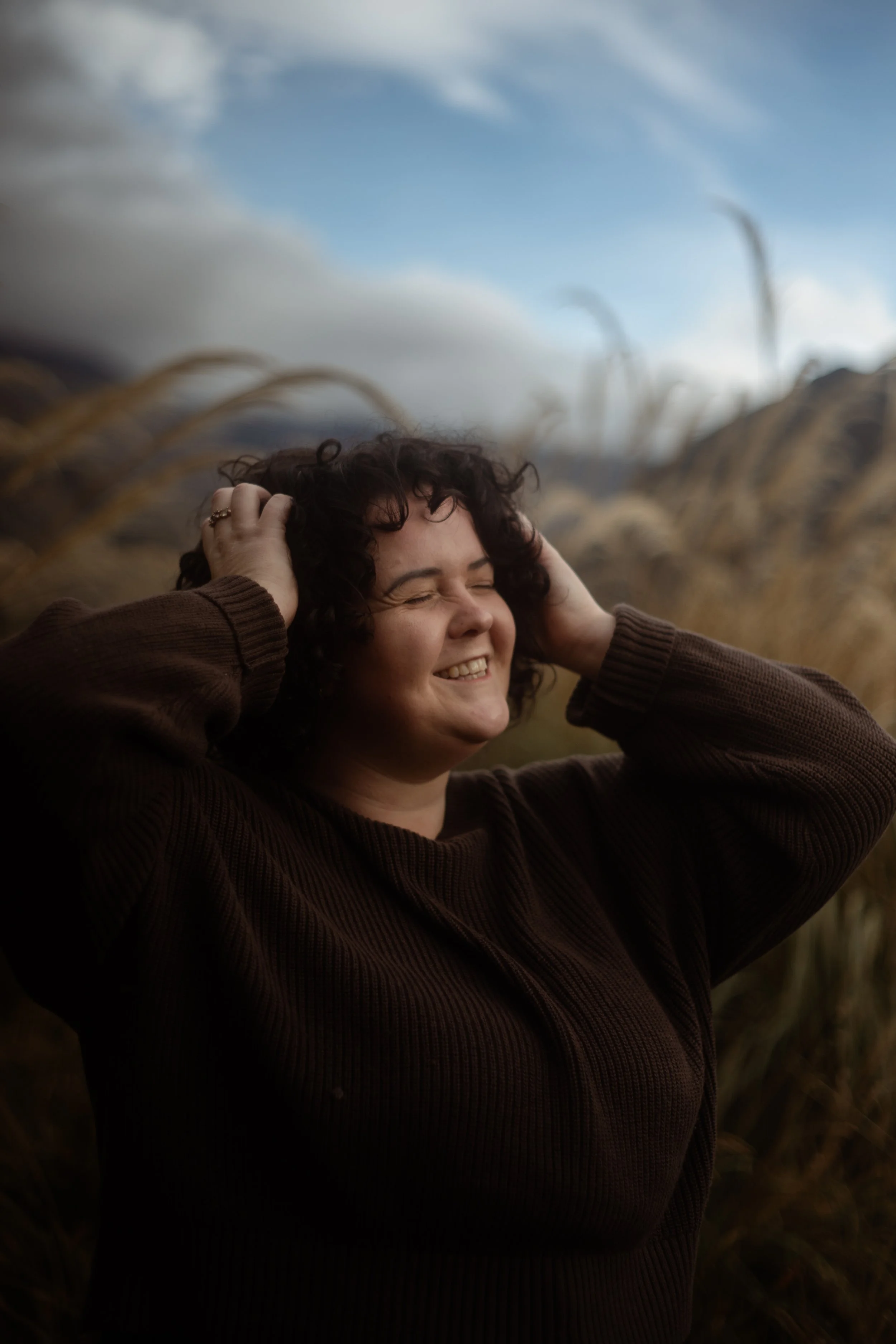 Girl with hands in her curly hair, in long grass