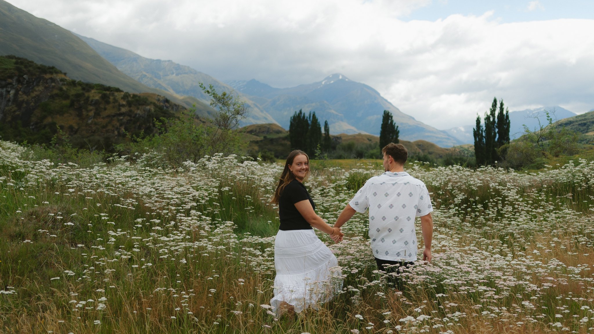 Couple walking in a field of long grass below the mountains in wanaka New Zealand