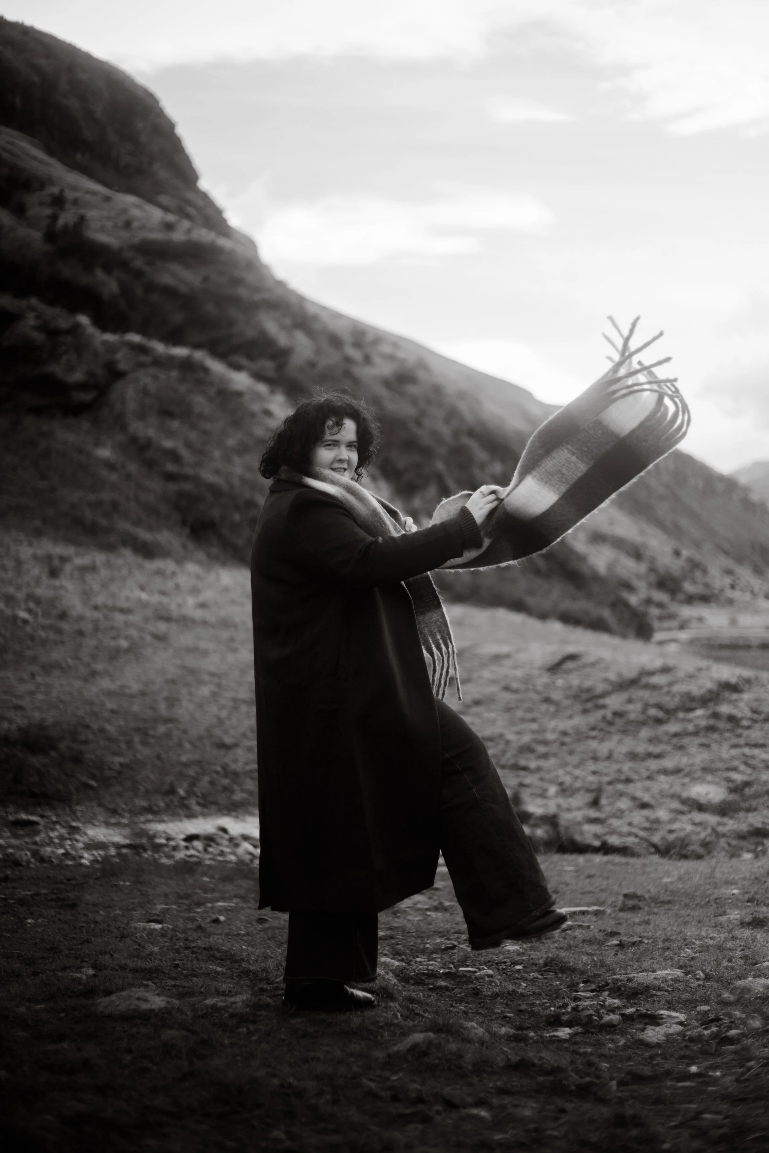 Girl wearing trench coat and scarf walking below wanaka mountains