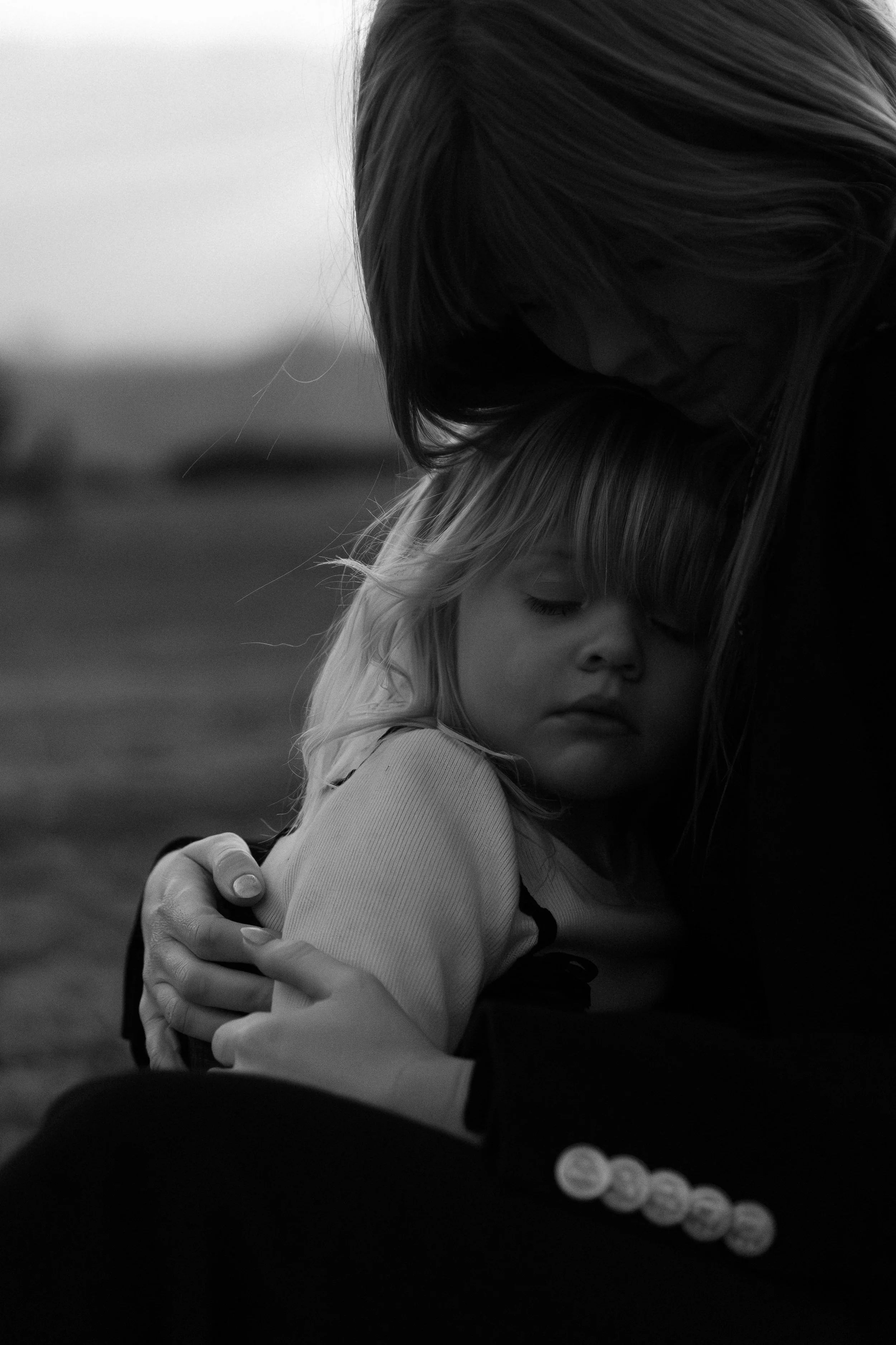 A woman and a young girl embracing outdoors, close-up shot in black and white.