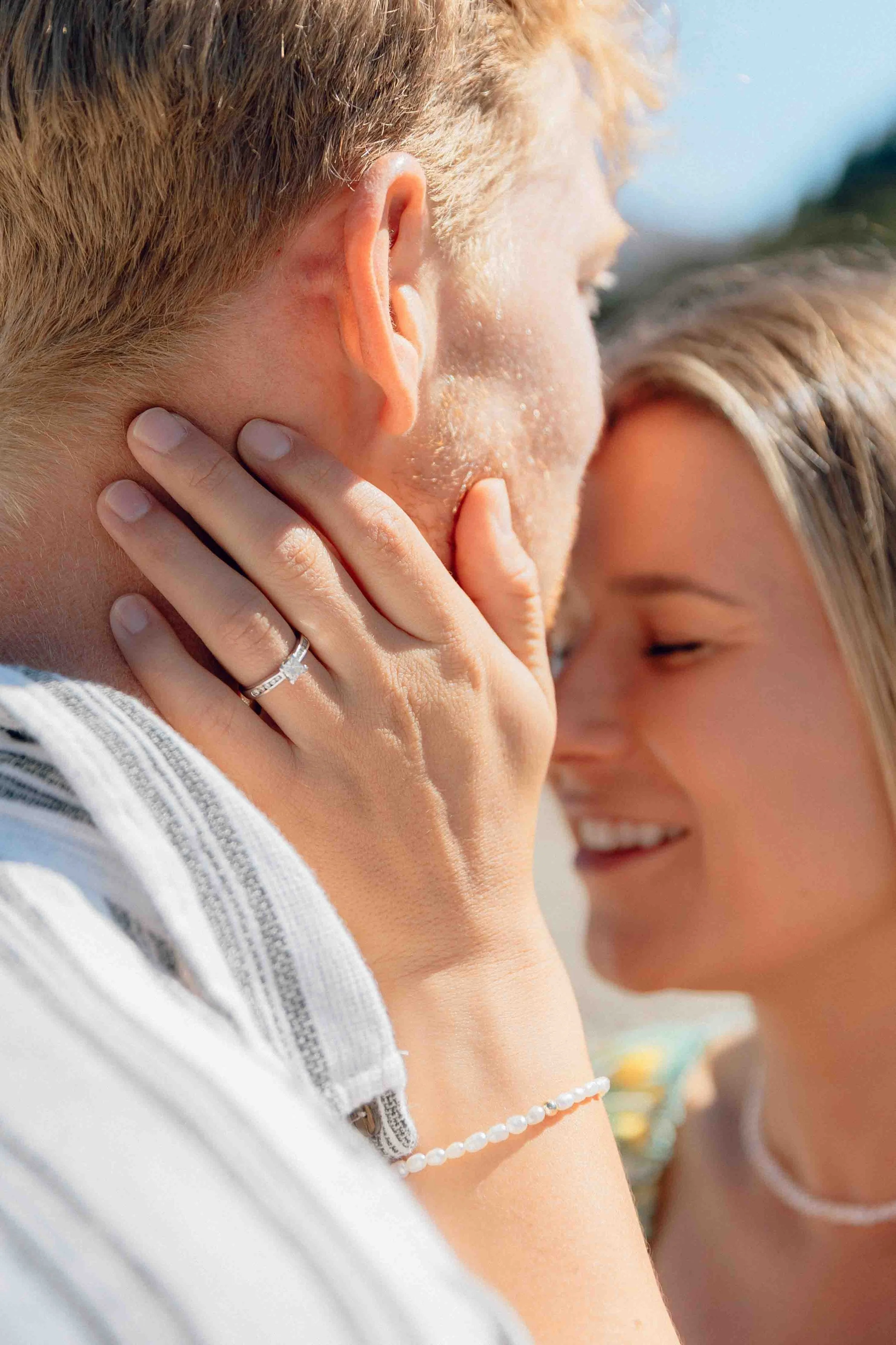 Close-up of a couple touching foreheads and smiling, outdoors, with sunlight shining on them.