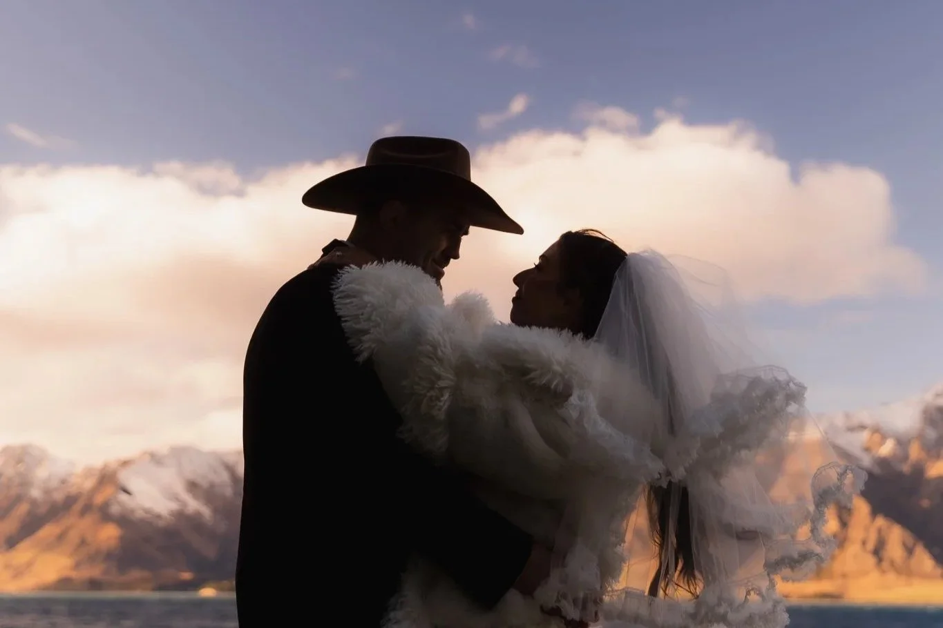 Couple embracing in wedding attire, with mountains of Lake Hāwea in the background
