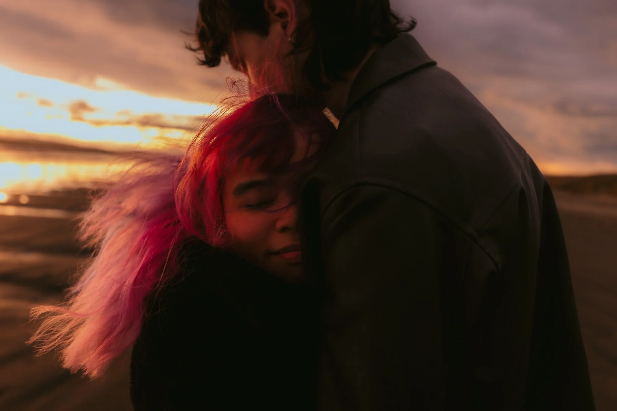 Couple embracing, female with pink hair on southland beach at sunset