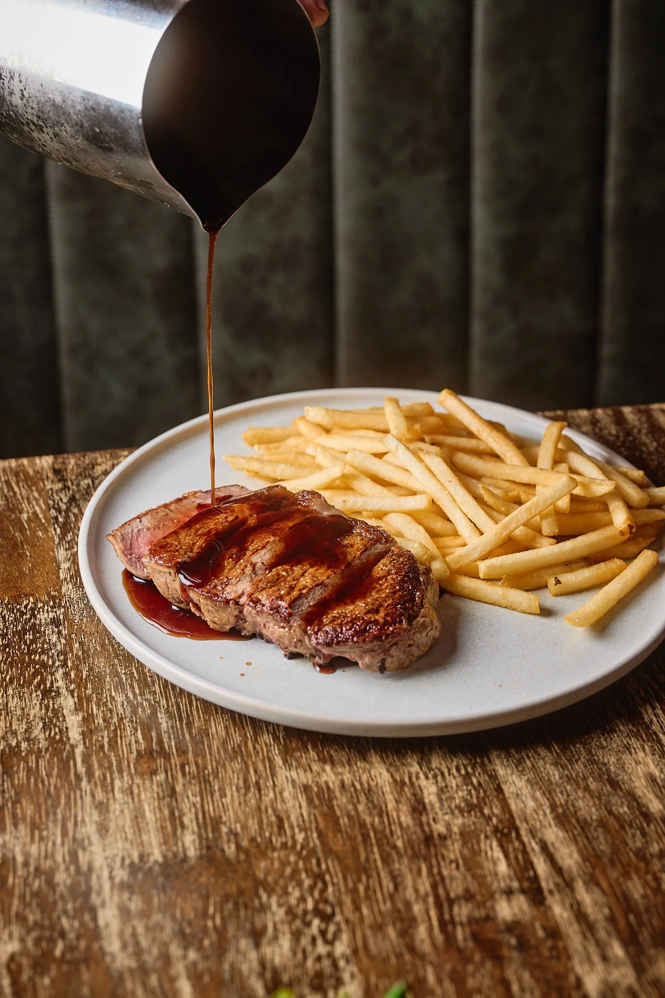 A plate of French fries and a grilled steak with gravy being poured over it.