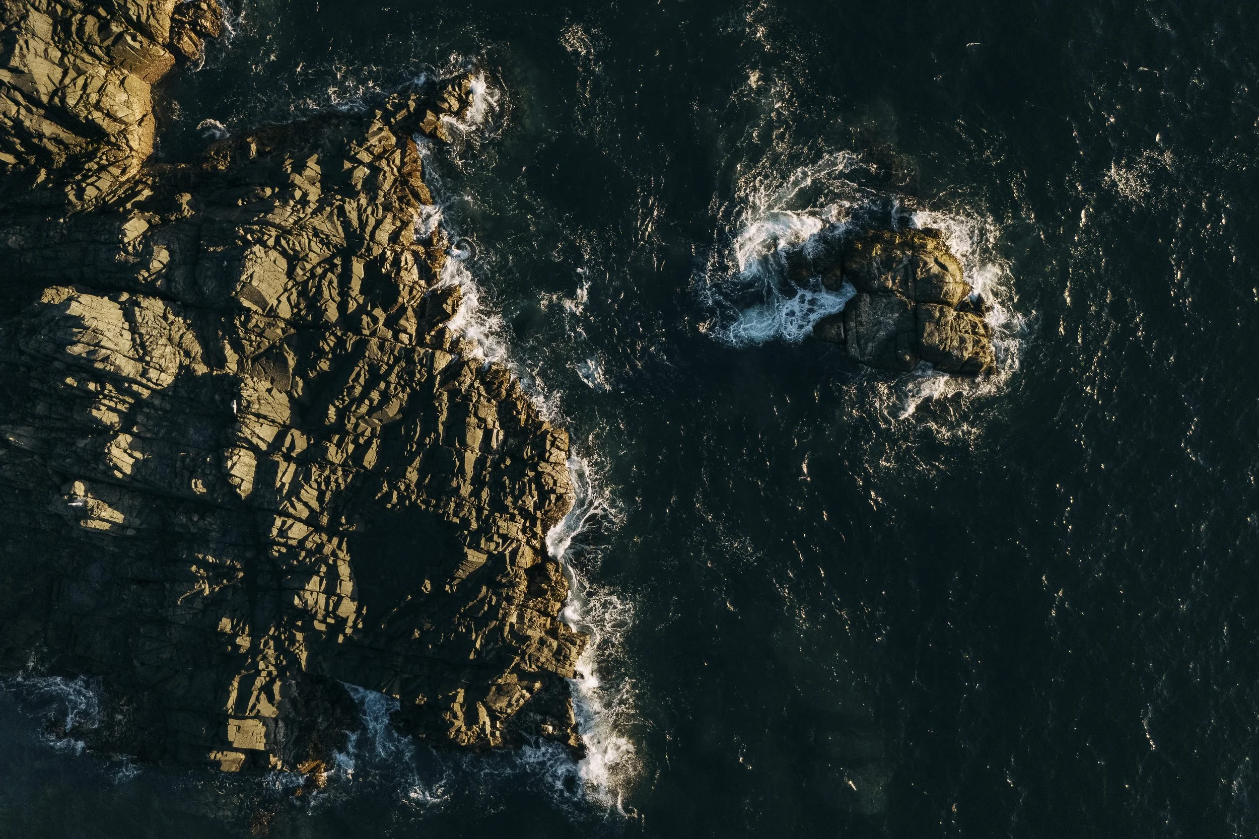 Aerial view of a rocky coastline with waves crashing against the rocks in the ocean.