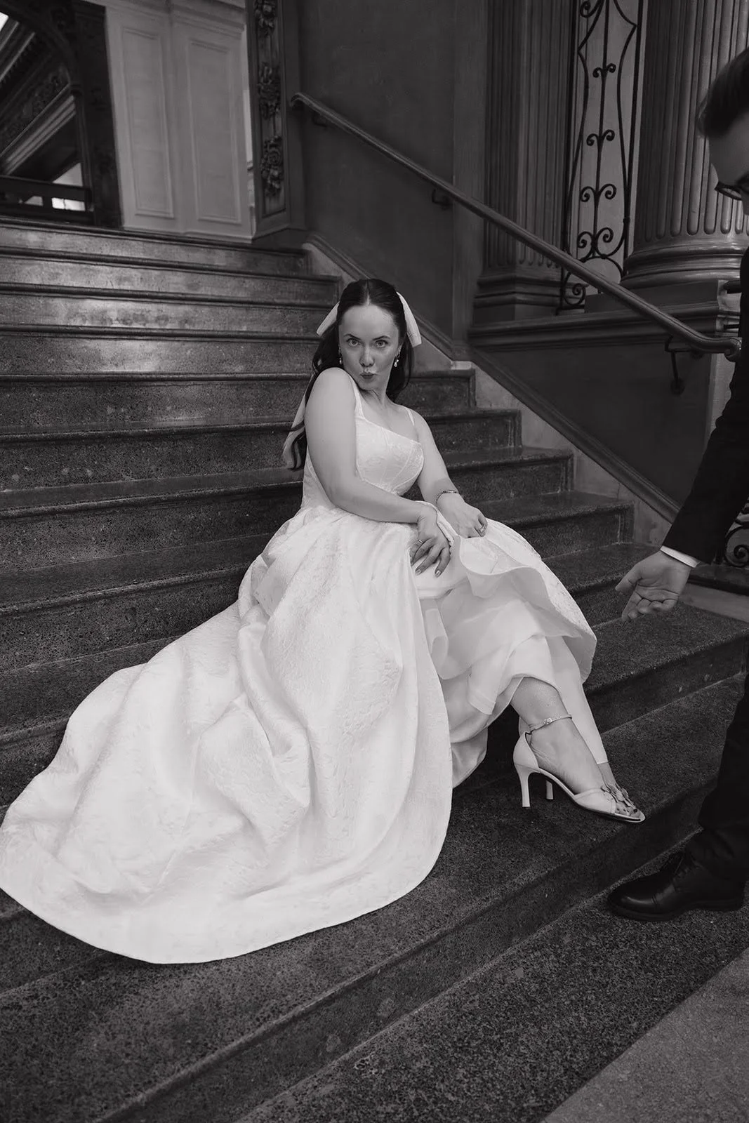 A woman in a wedding dress sitting on a staircase making a silly face.