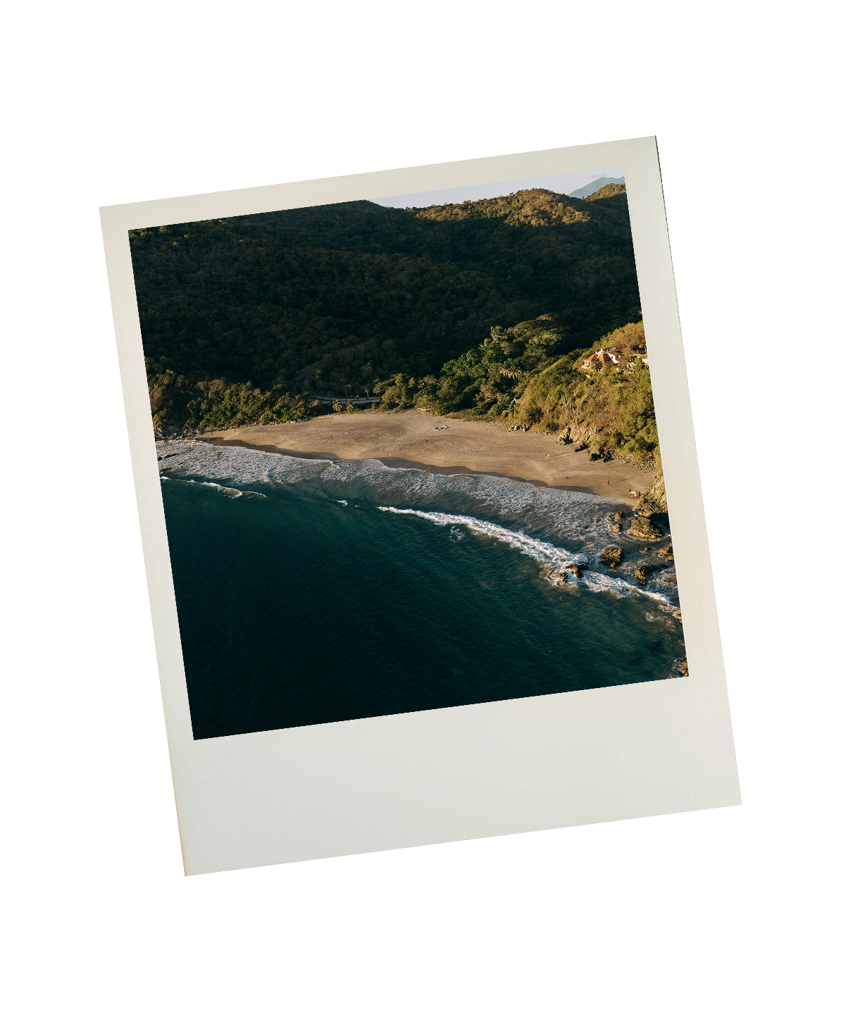 Aerial view of a Mexican beach with waves crashing on the shore, surrounded by green hills and mountains in the background.
