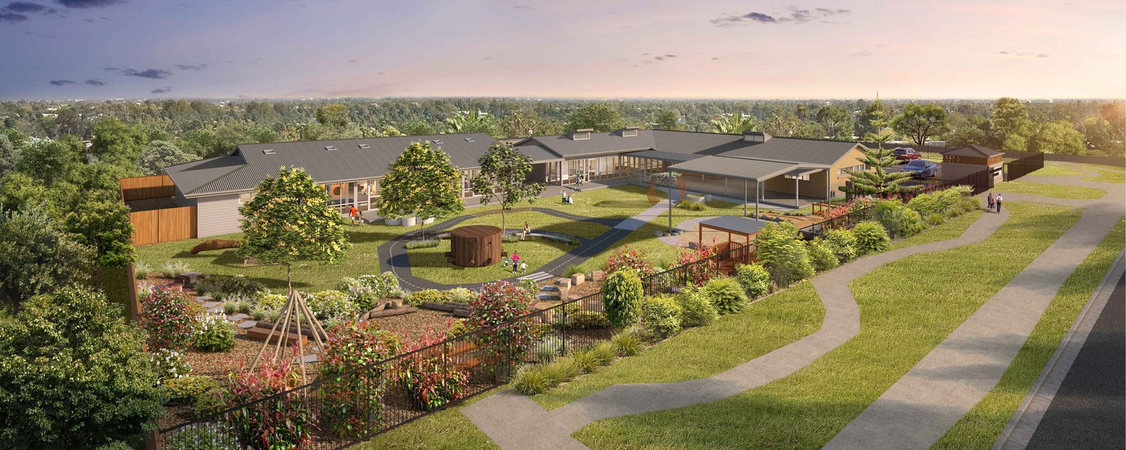 A large, modern community center with surrounding landscaped gardens, walking paths, trees, and outdoor recreational areas, including a playground and seating areas, during sunset.