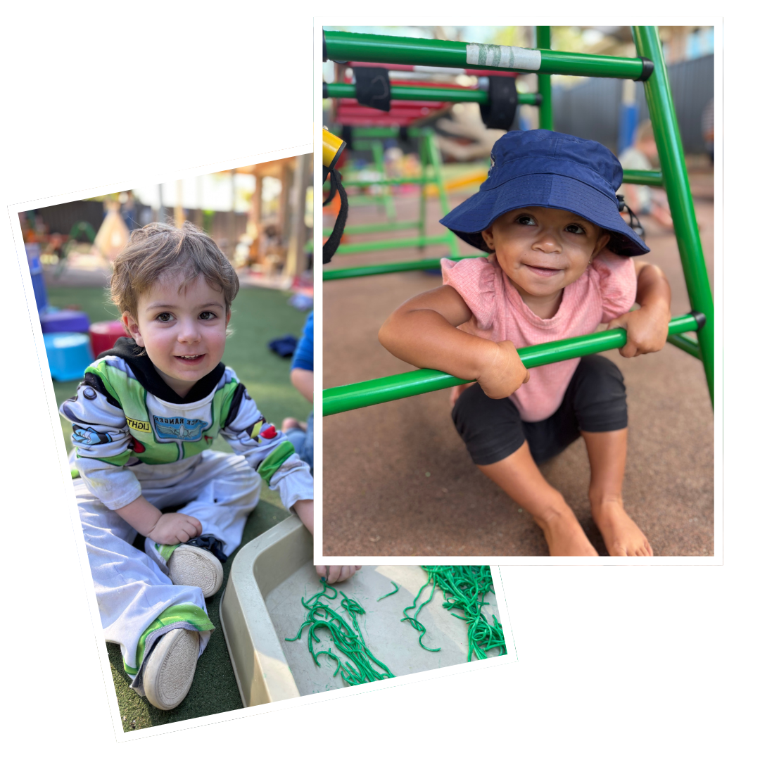 Two young children playing outside at a playground, one sitting on the ground with themed paper strips, and the other crawling through a green metal structure, wearing a blue sun hat and pink shirt.